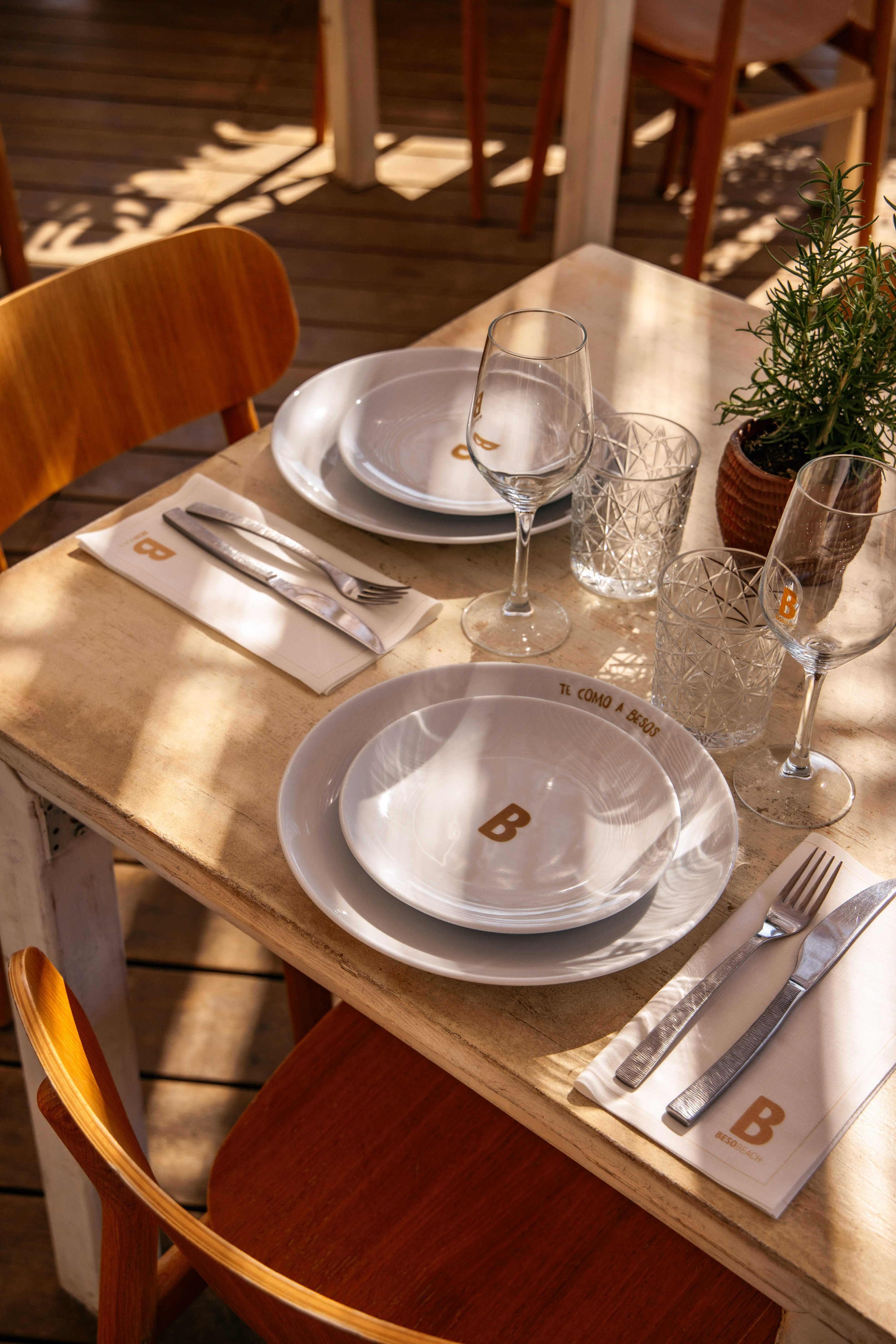 Sunny Beso Beach restaurant table setting with white plates, glasses, and rosemary.