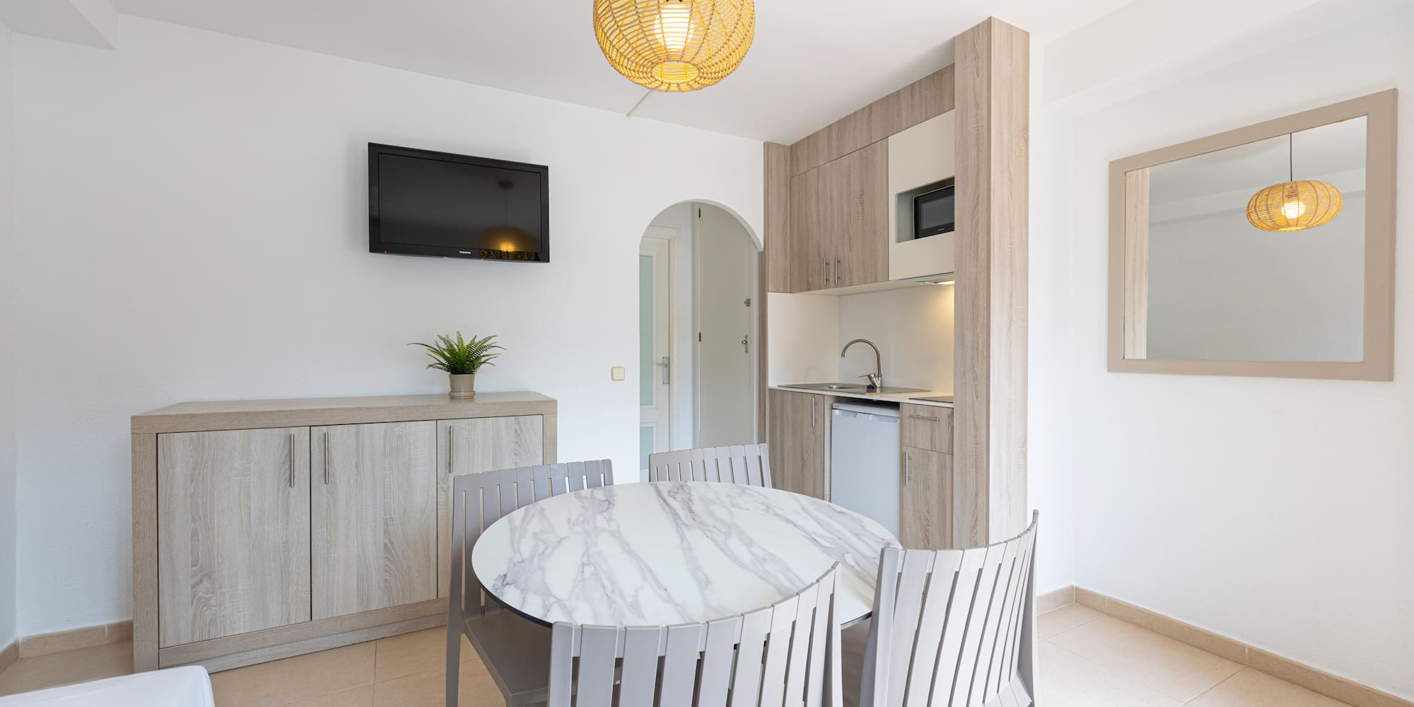 Bright studio apartment with modern kitchenette, round dining table, and TV.