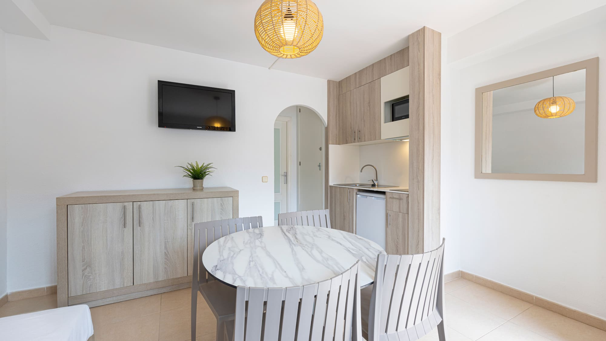 Hotel studio apartment with kitchenette, round dining table, and wall-mounted TV.