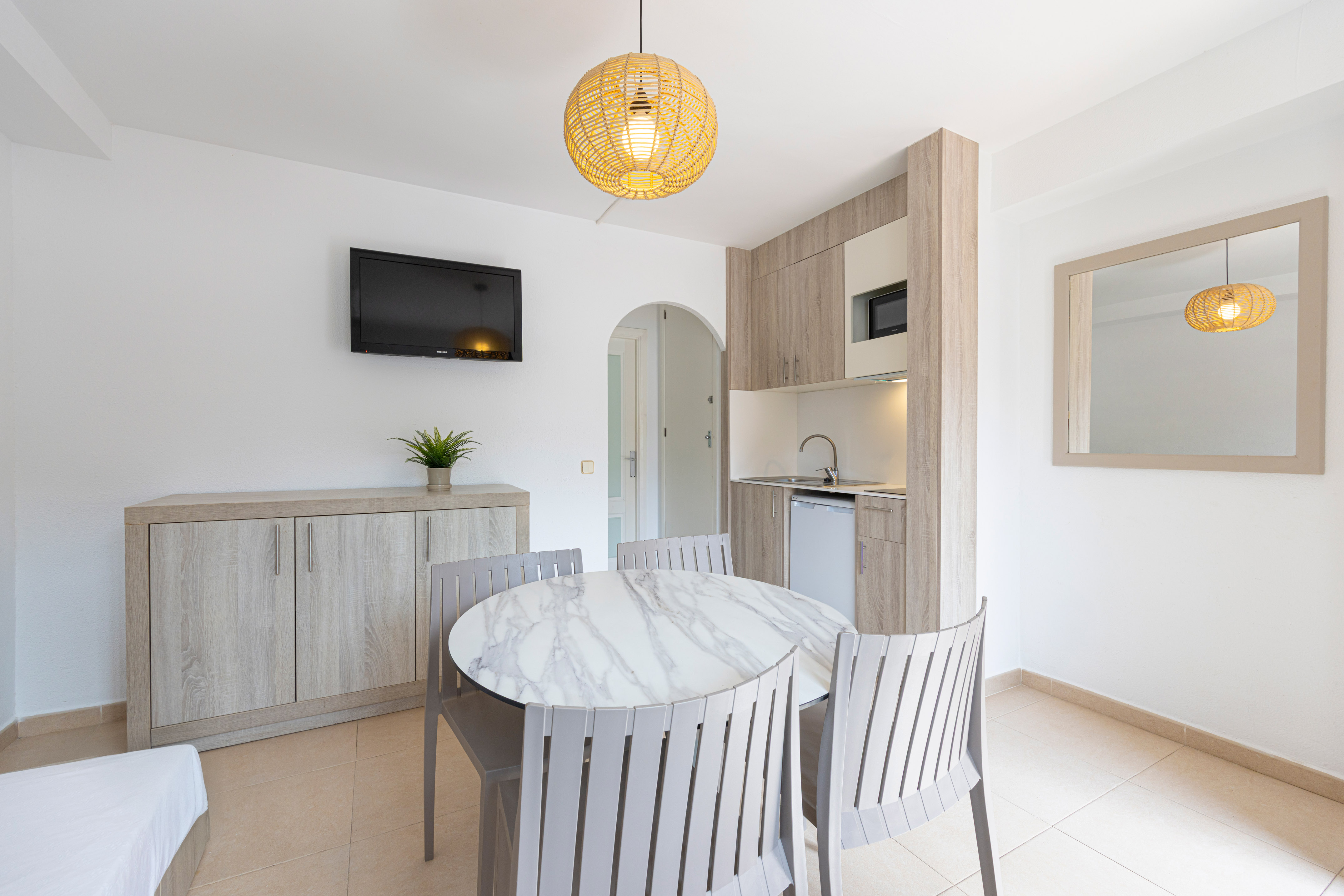 Bright studio apartment with modern kitchenette, round dining table, and TV.