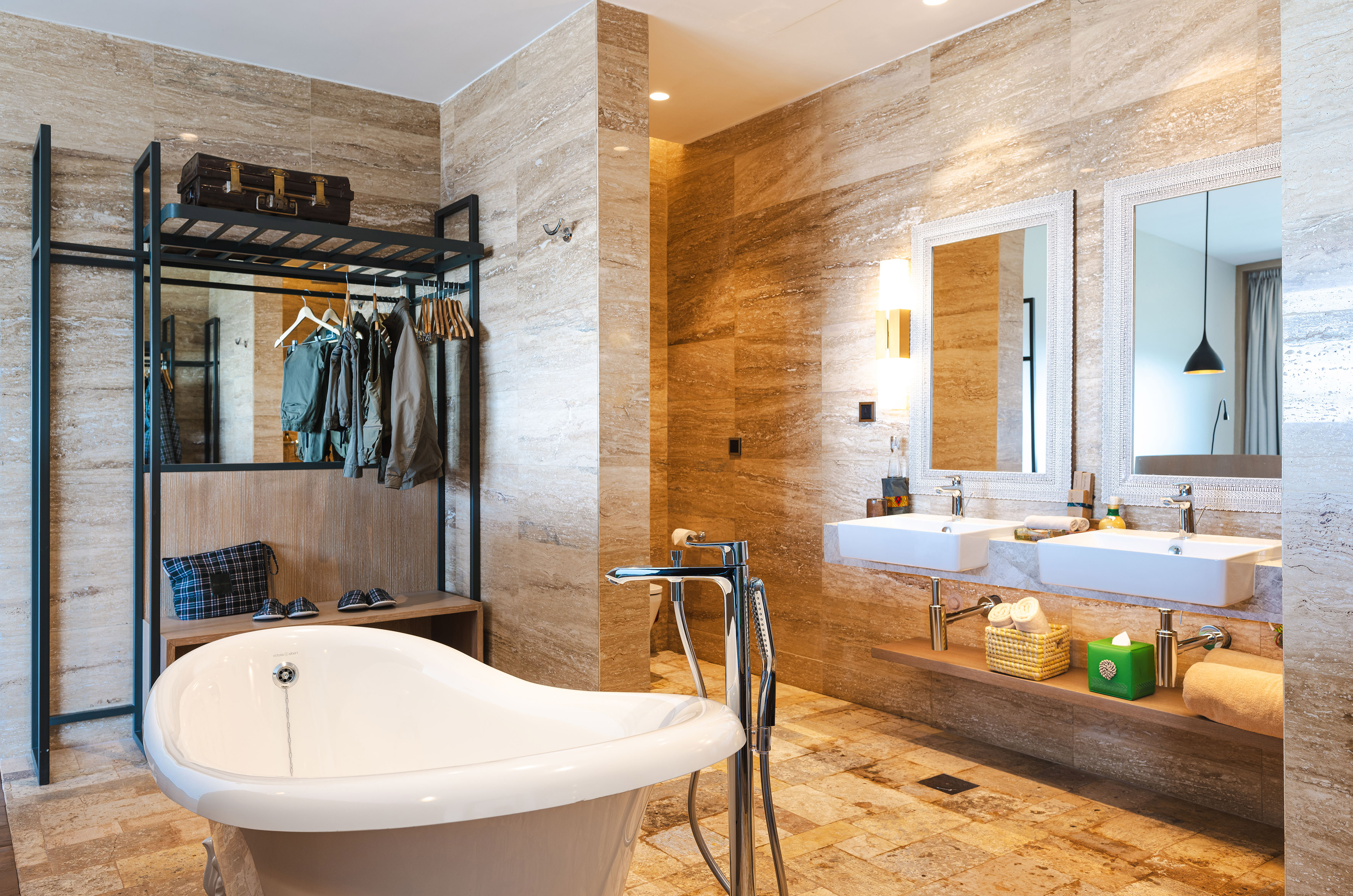 Luxury bathroom with freestanding tub, double vanity, stone tiles, and open closet.