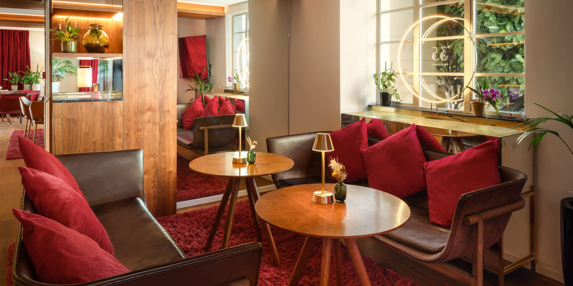 Cozy hotel lounge with red carpet, leather seating, wood tables, warm lighting.