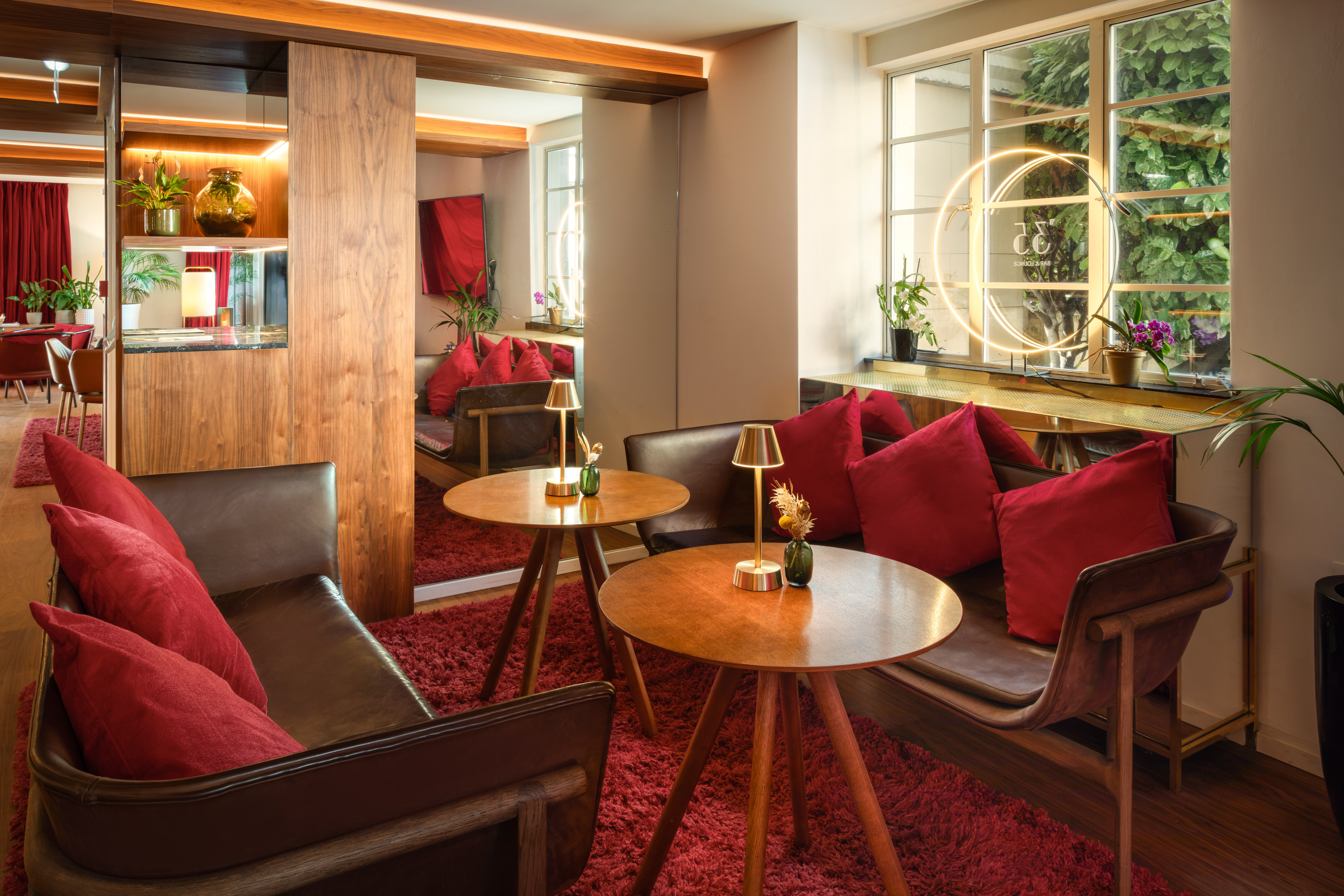 Cozy hotel lounge with red carpet, leather seating, wood tables, warm lighting.