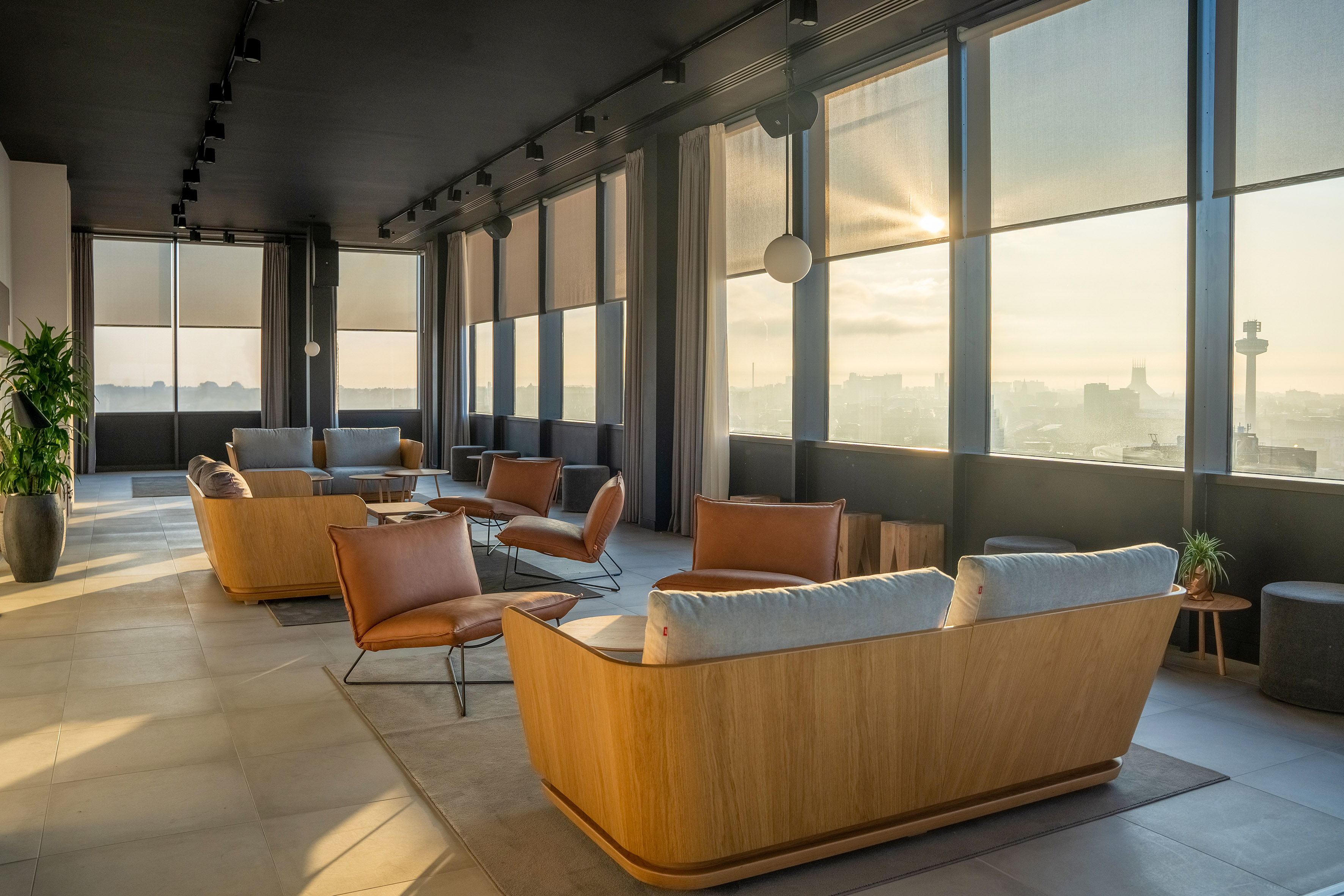 Modern lounge with panoramic Liverpool city skyline at sunset, comfortable seating.