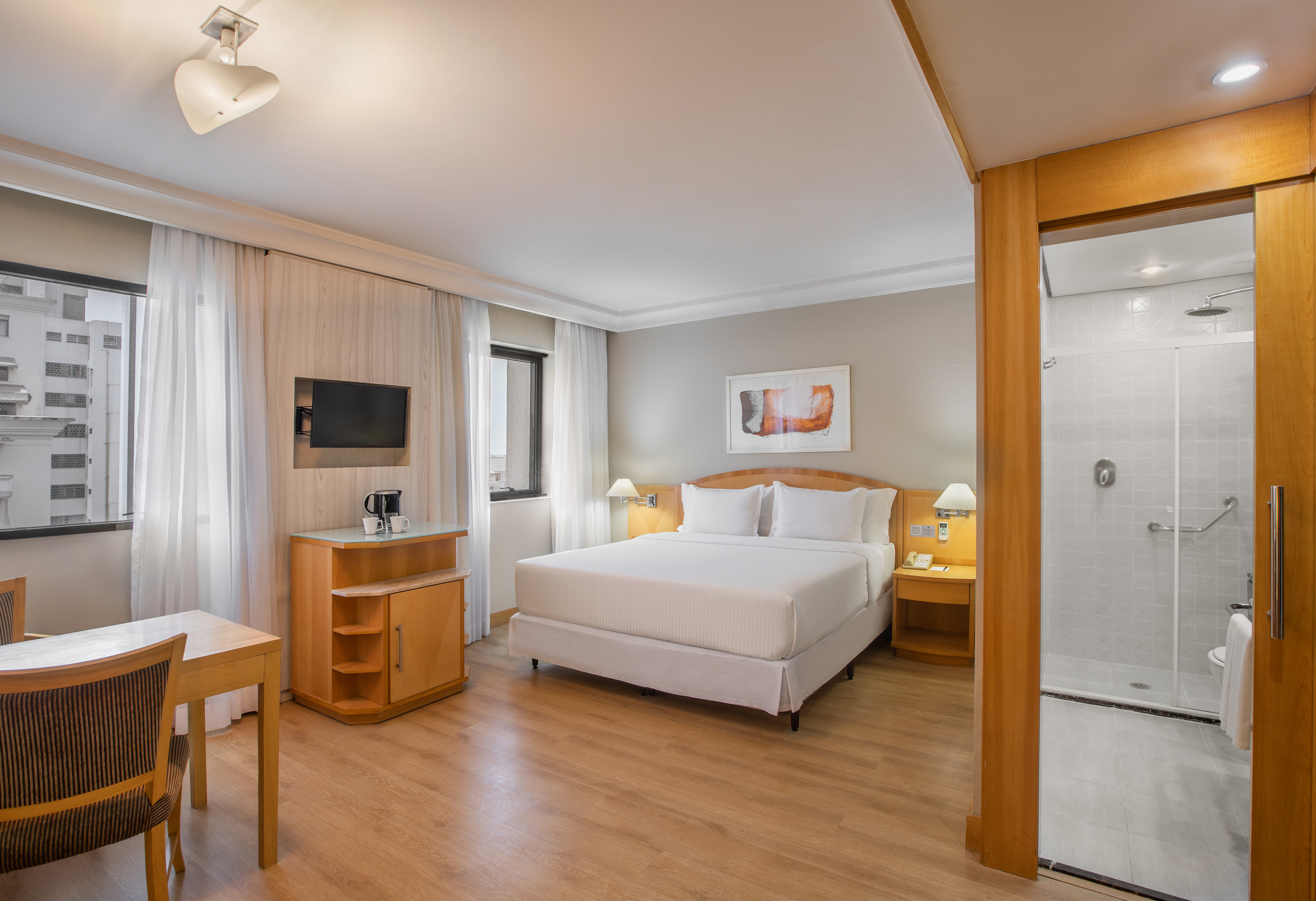 Modern hotel room with queen bed, TV, work table, and private tiled bathroom.