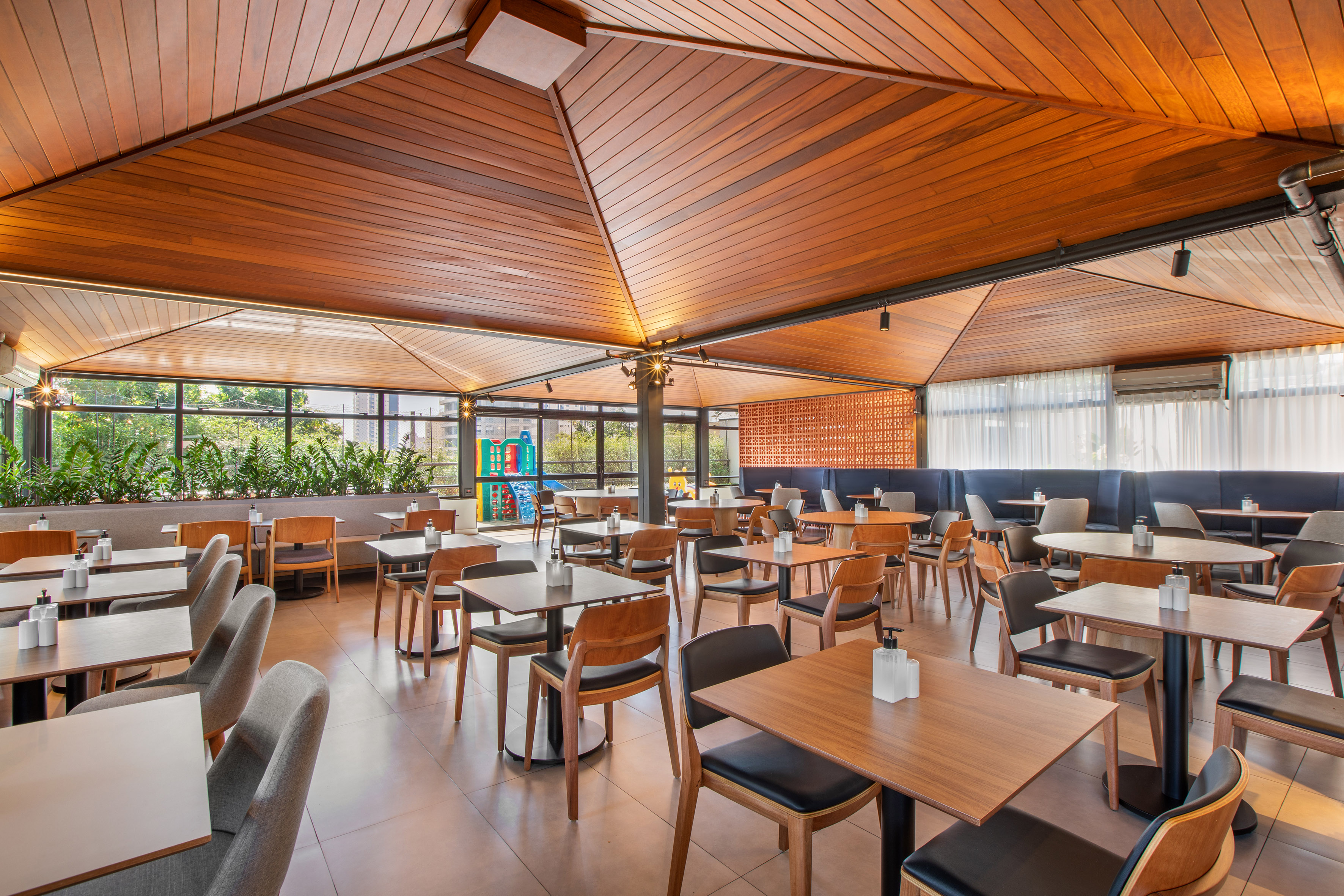 Modern restaurant interior with wooden ceiling, large windows, and dining tables.