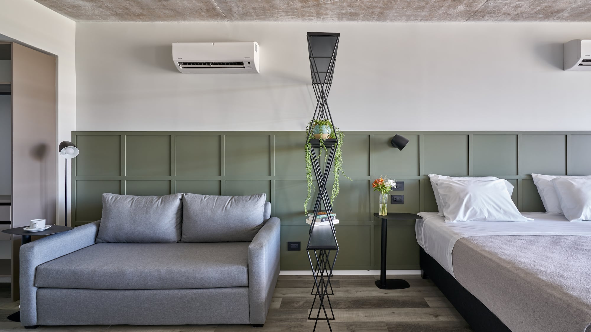 Modern hotel room with grey sofa bed, green paneled wall, concrete ceiling.
