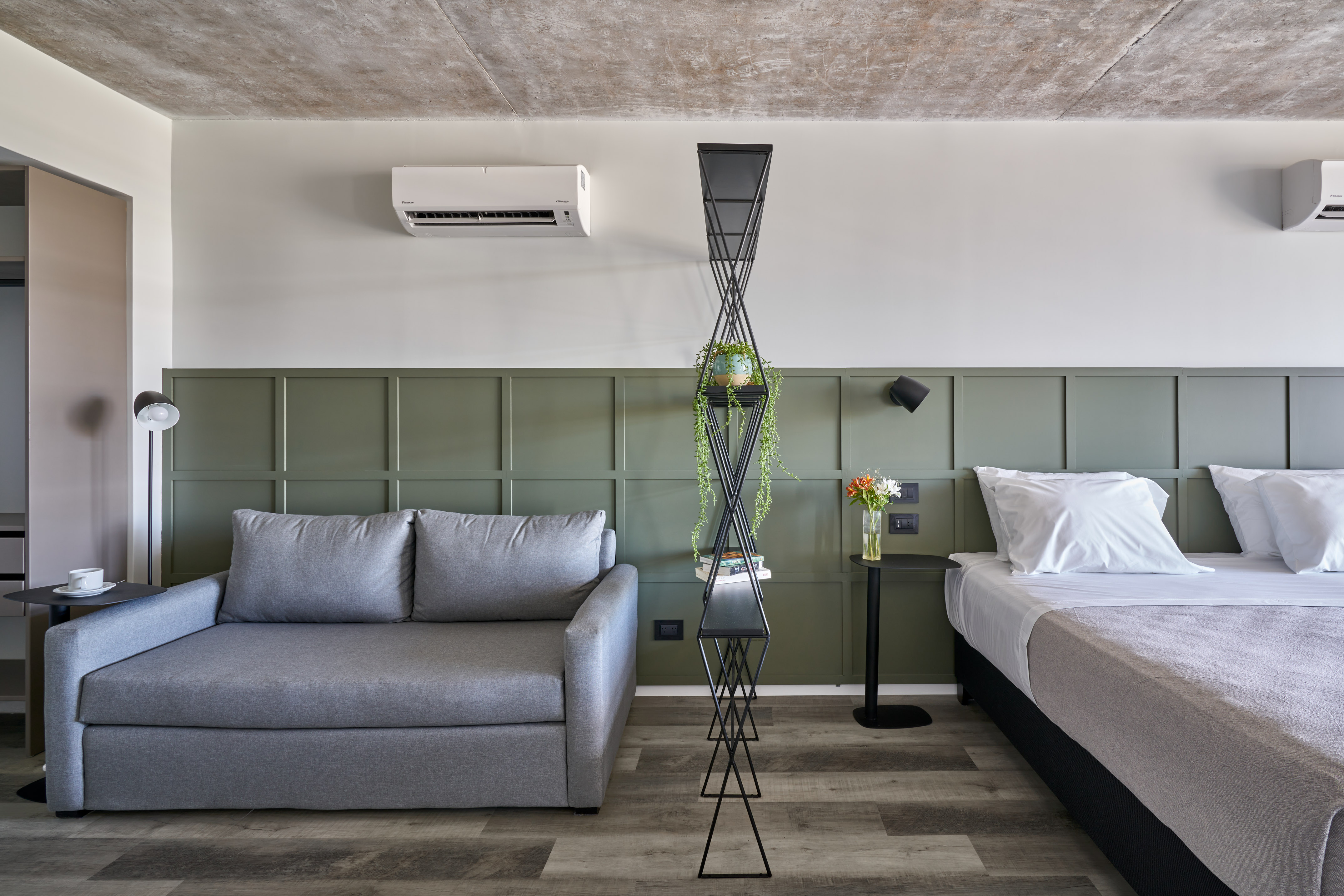 Modern hotel room with grey sofa bed, green paneled wall, concrete ceiling.