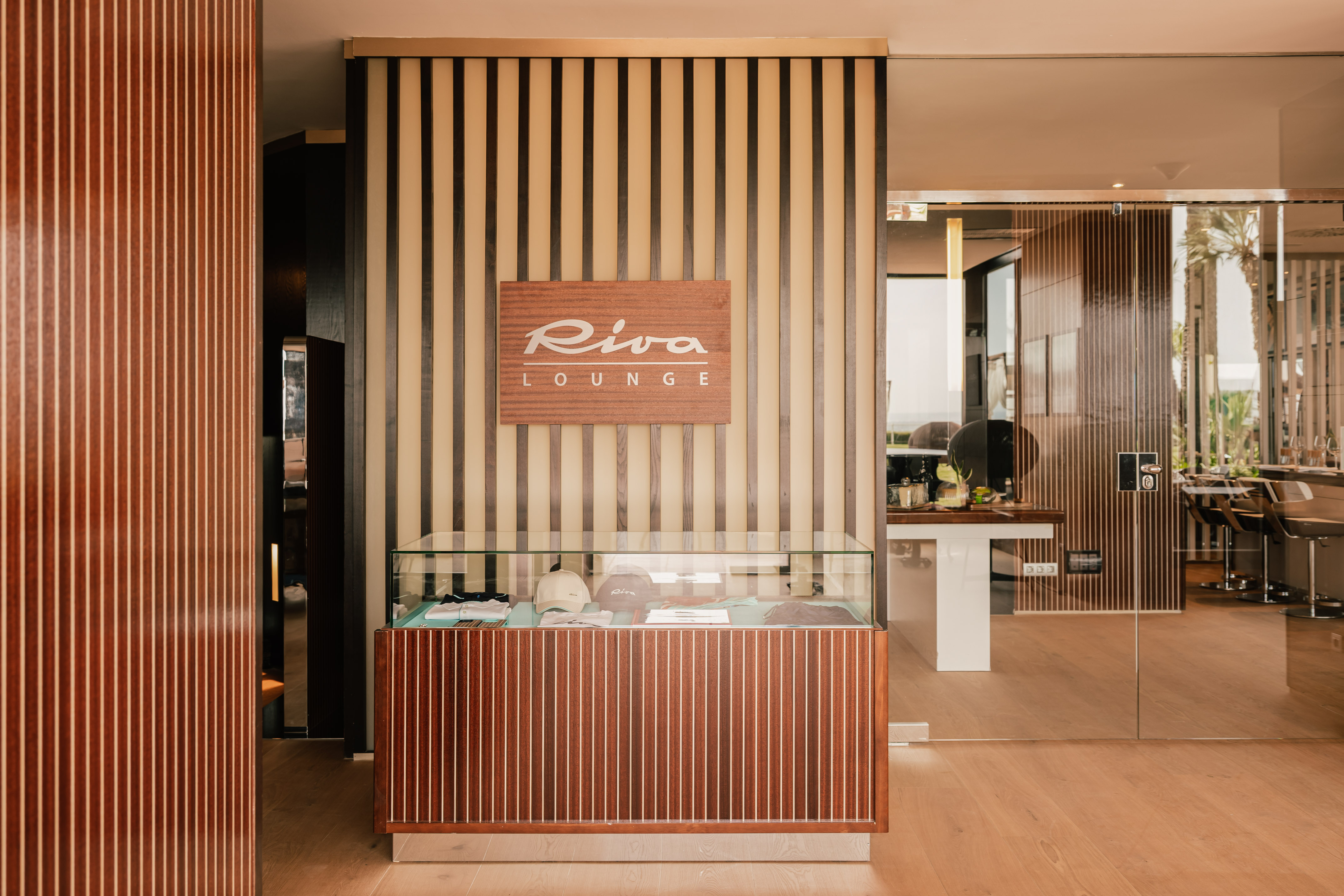 Riva Lounge entrance, wooden sign, glass display, and slatted wall decor.
