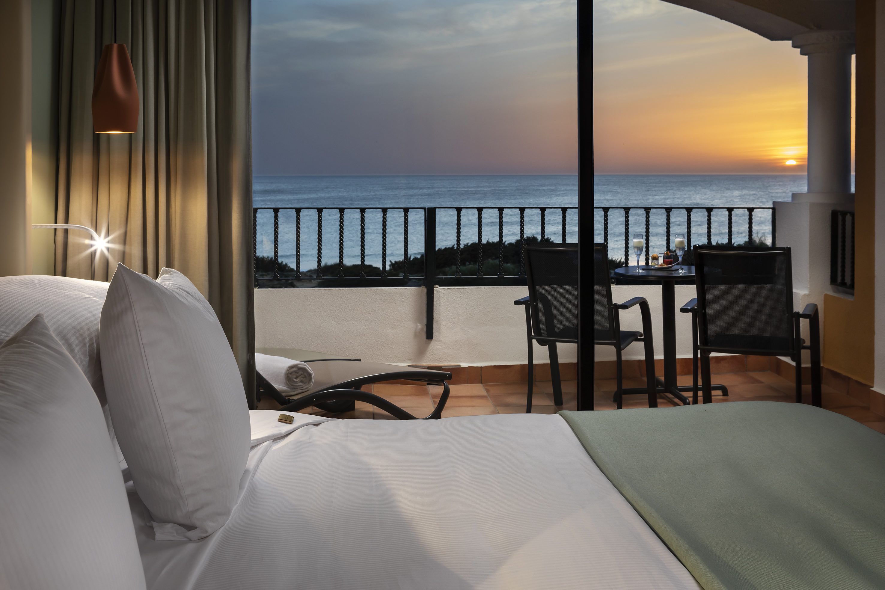 Luxury hotel room with ocean view balcony at sunset.