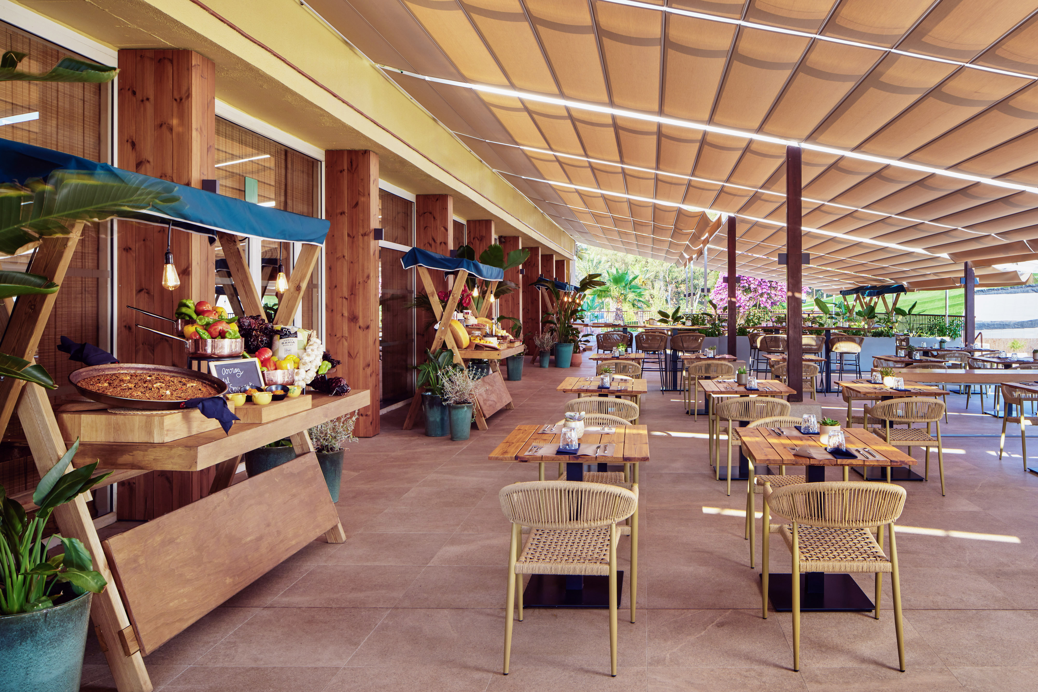 Shaded outdoor restaurant buffet with paella, fresh food, and patio seating.