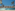 Resort swimming pool with palm trees, sun umbrellas, and yacht marina.