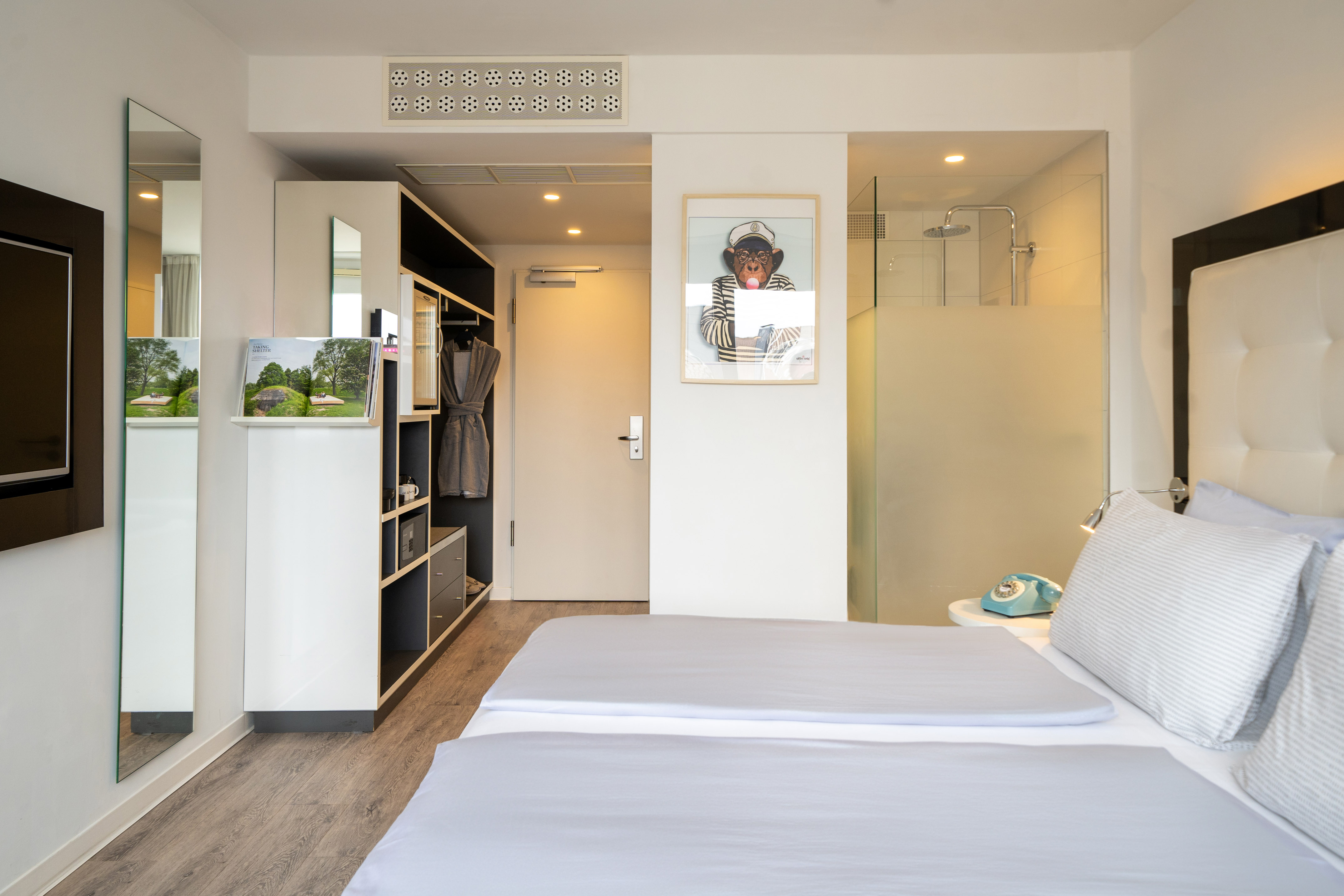 Modern hotel guest room with bed, integrated storage, TV, and monkey print.