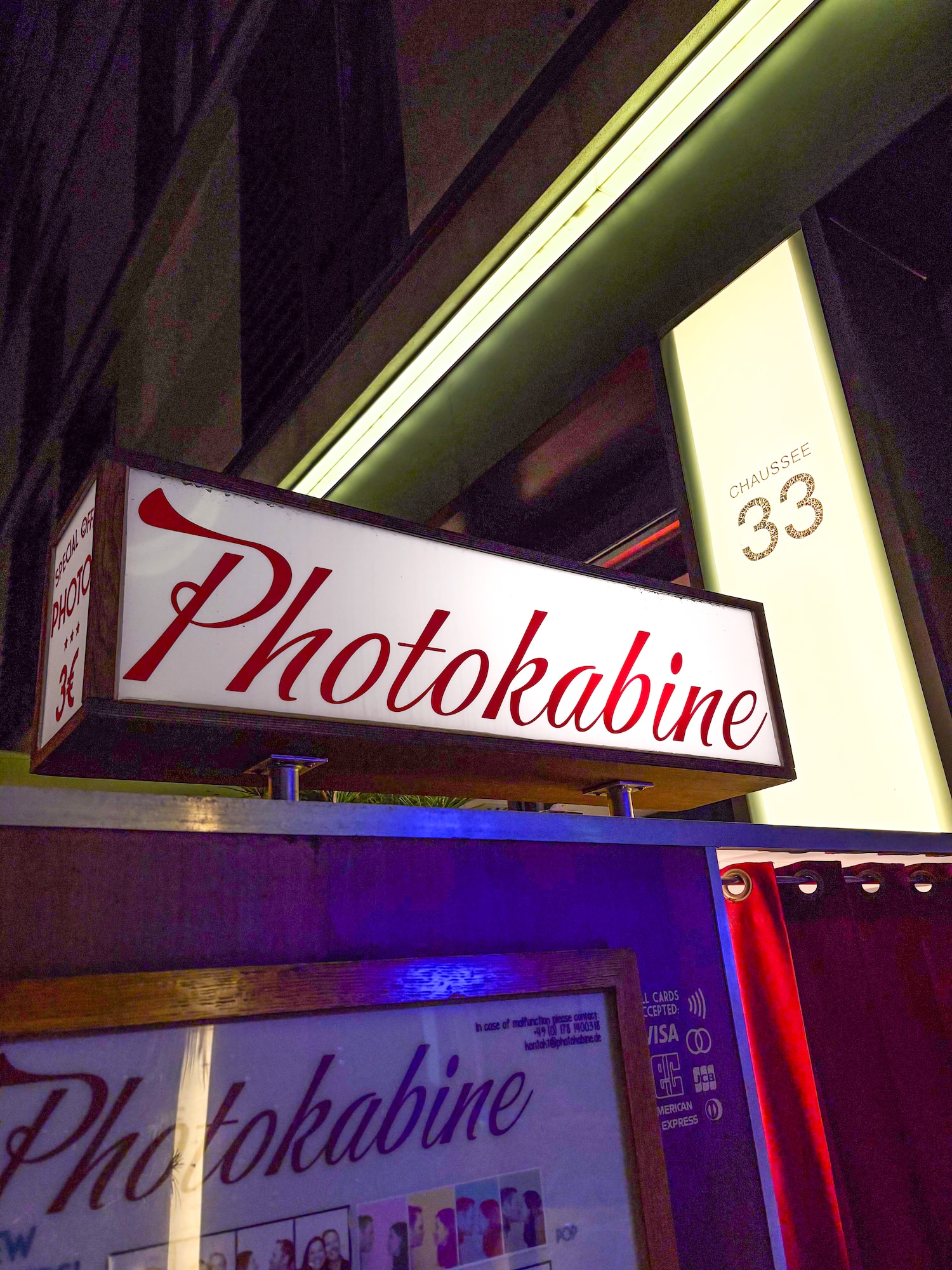 Glowing 'Photokabine' sign, street photo booth with 'Chaussée 33' number.