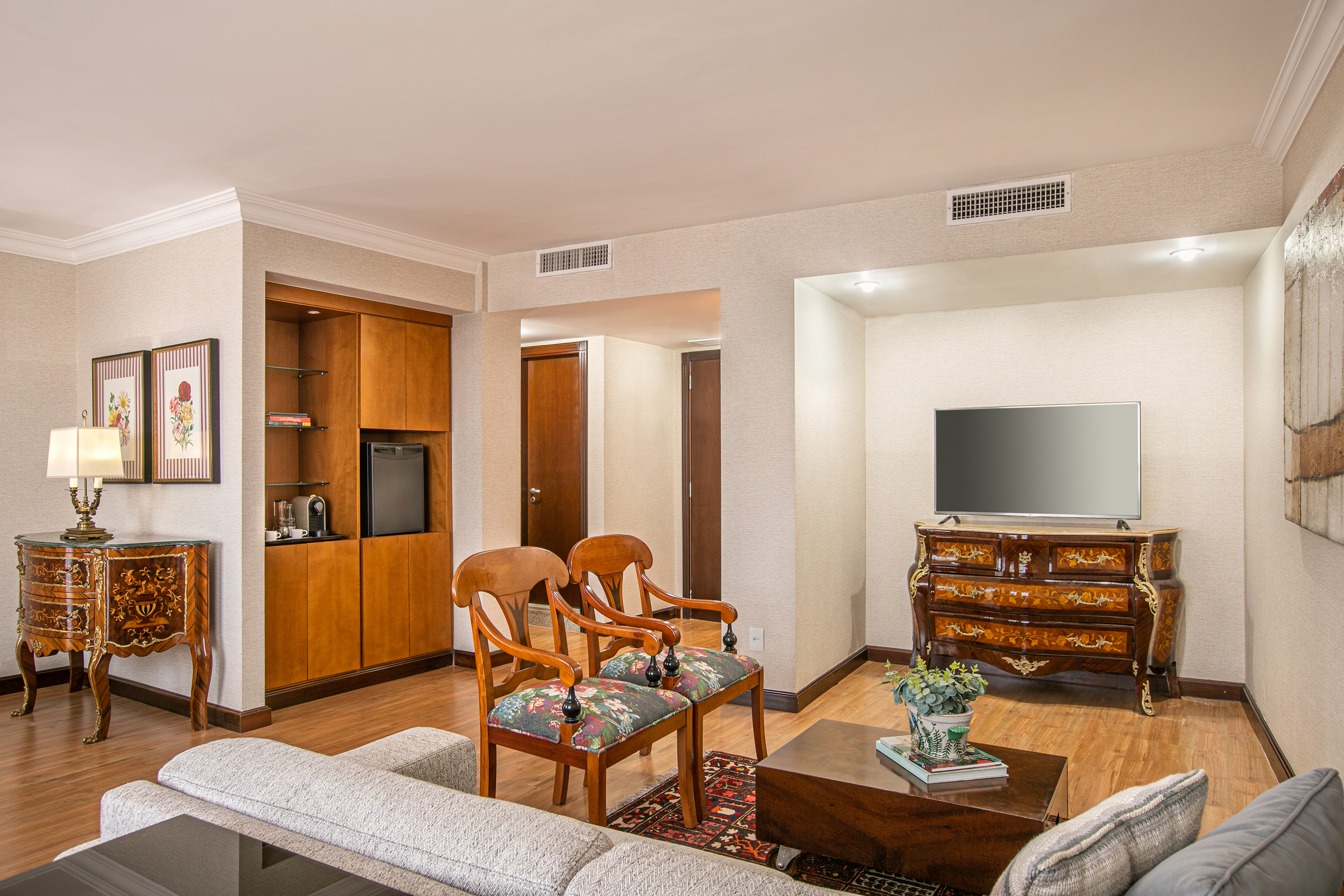 Elegant hotel suite living room with classic furniture, sofa, TV, and built-in minibar.