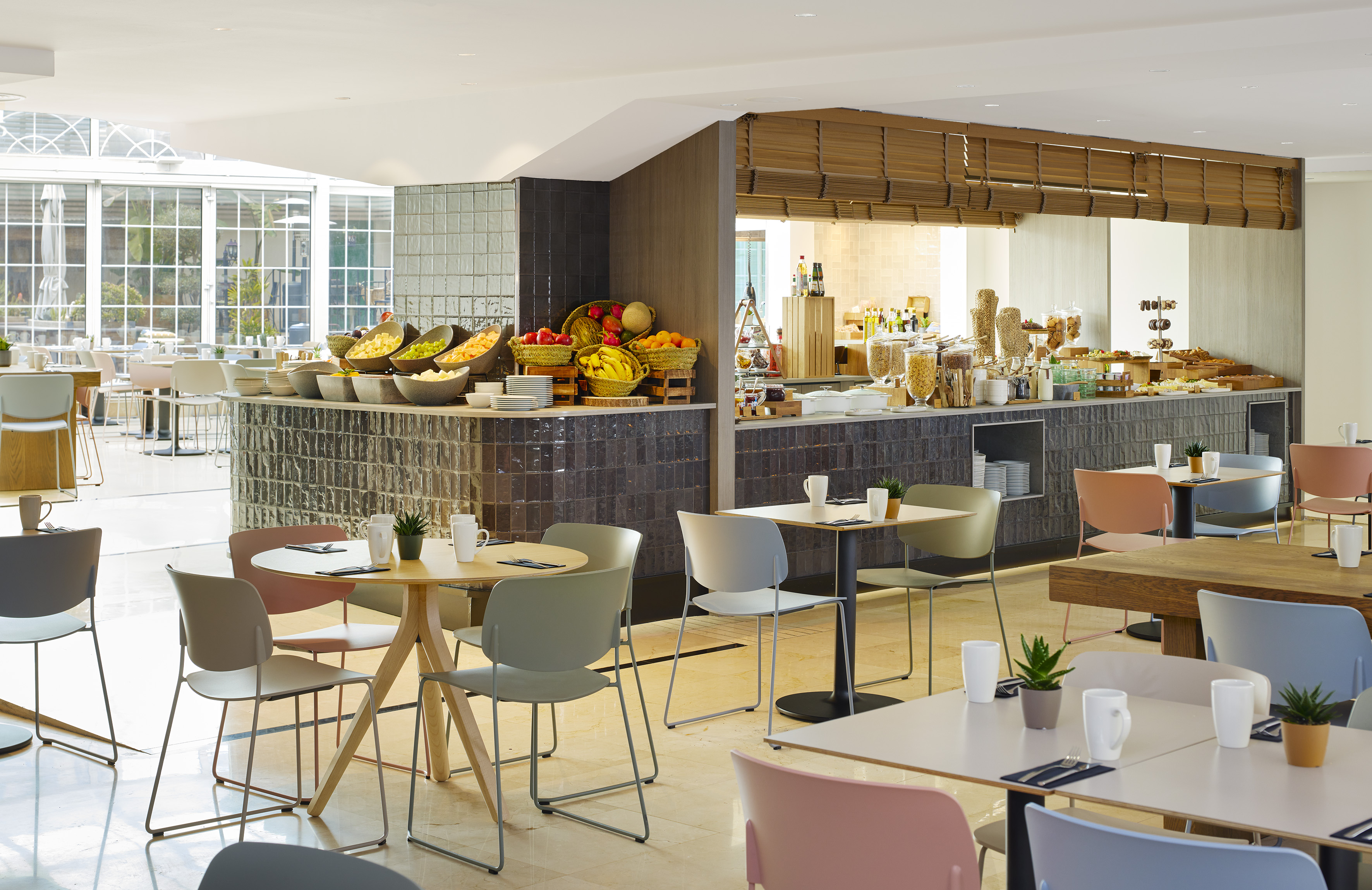 Modern hotel dining area with a breakfast buffet and fresh fruit.