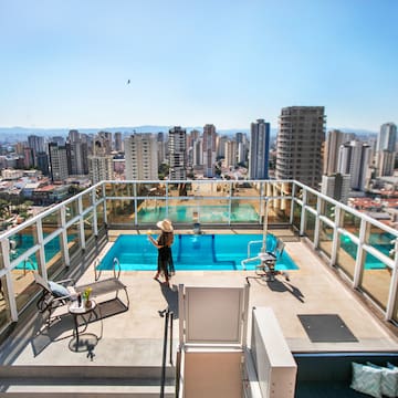 a woman standing on a rooftop with a pool and a city in the background