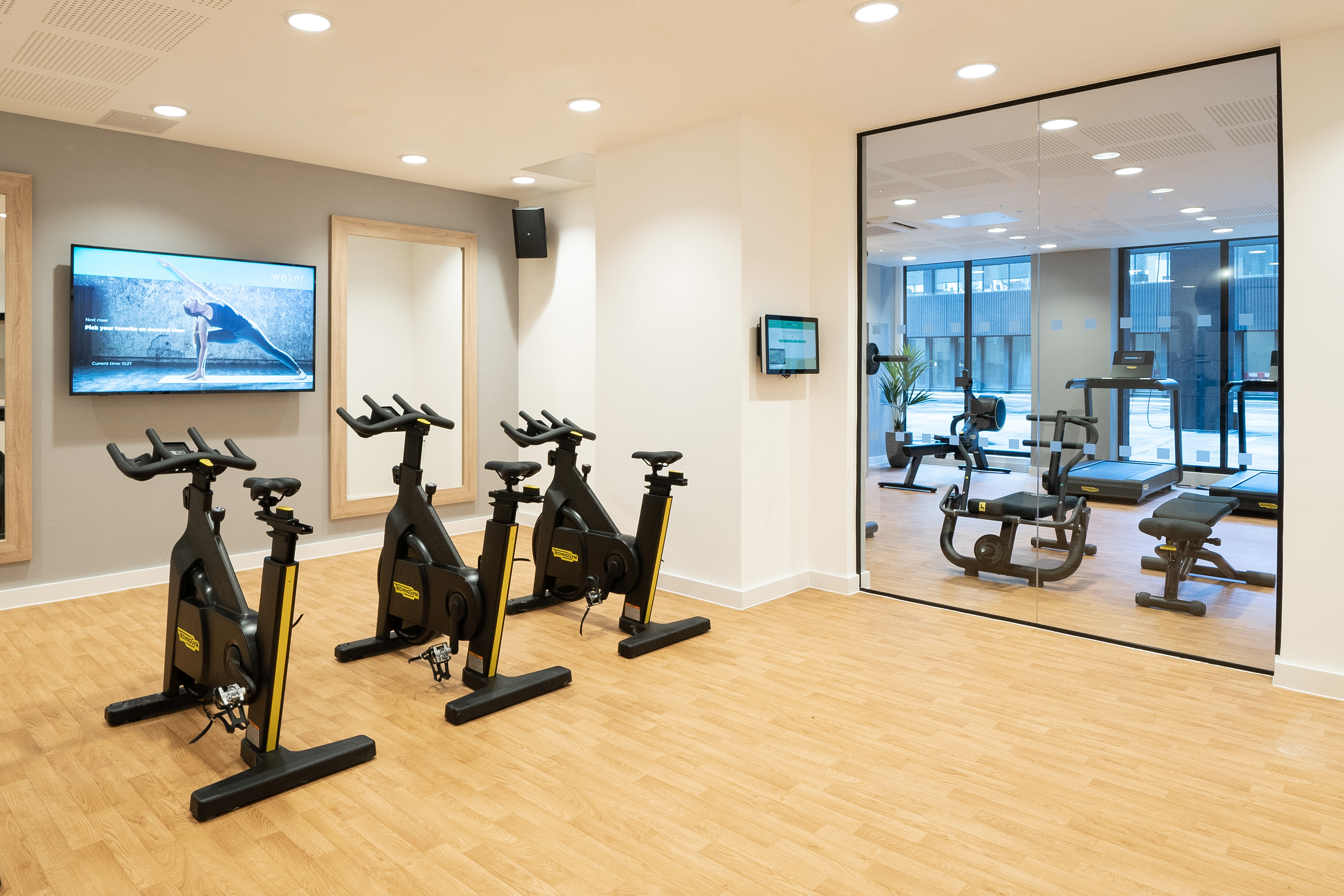 Fitness center with spin bikes, virtual yoga on screen, and exercise equipment.