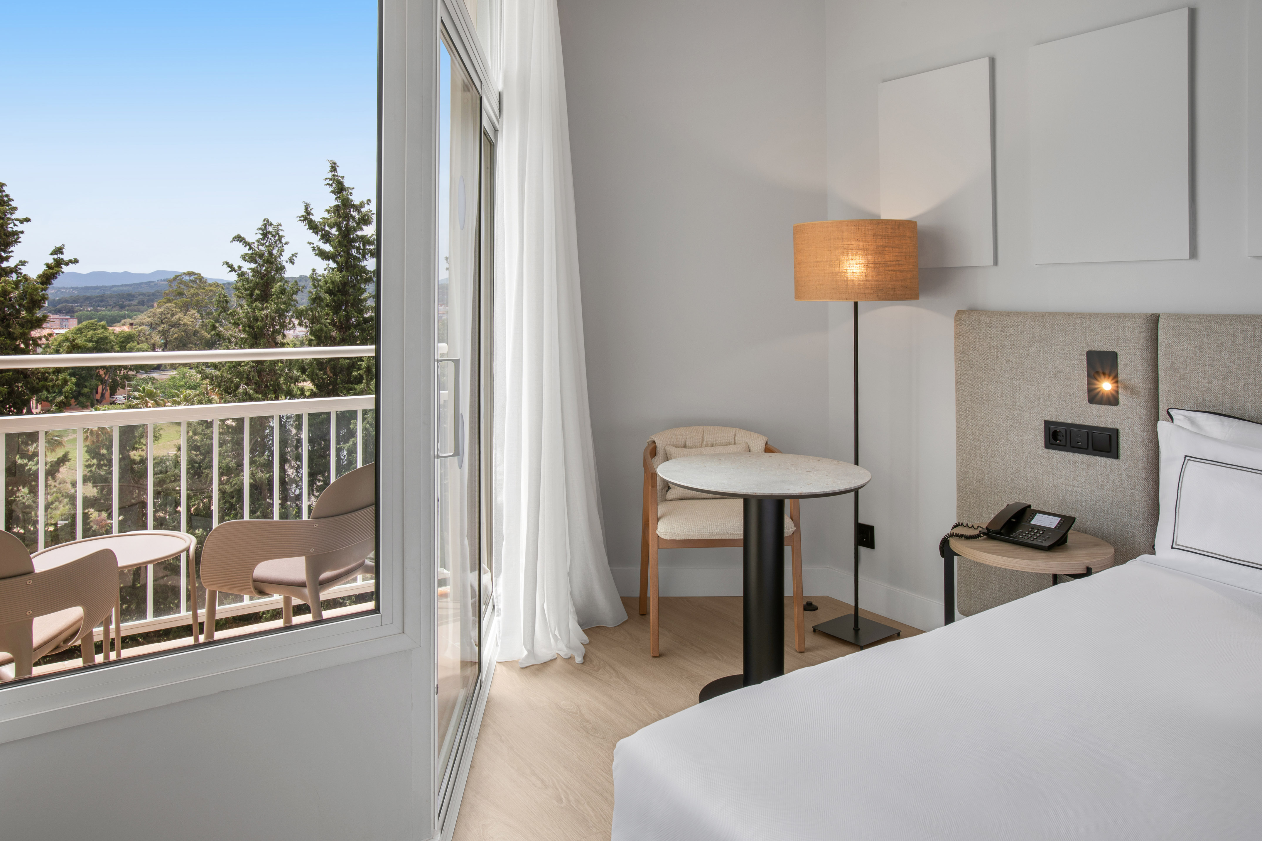 Bright hotel room with balcony, outdoor seating, and scenic nature views.