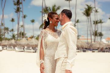 a man and woman in white dress standing on a beach