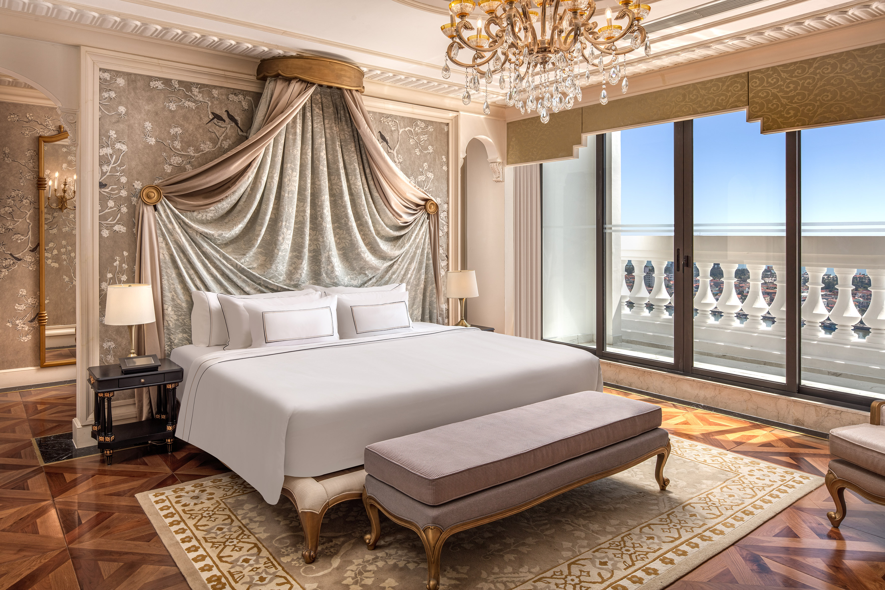 Elegant hotel bedroom with canopy bed, balcony, and ornate chandelier.
