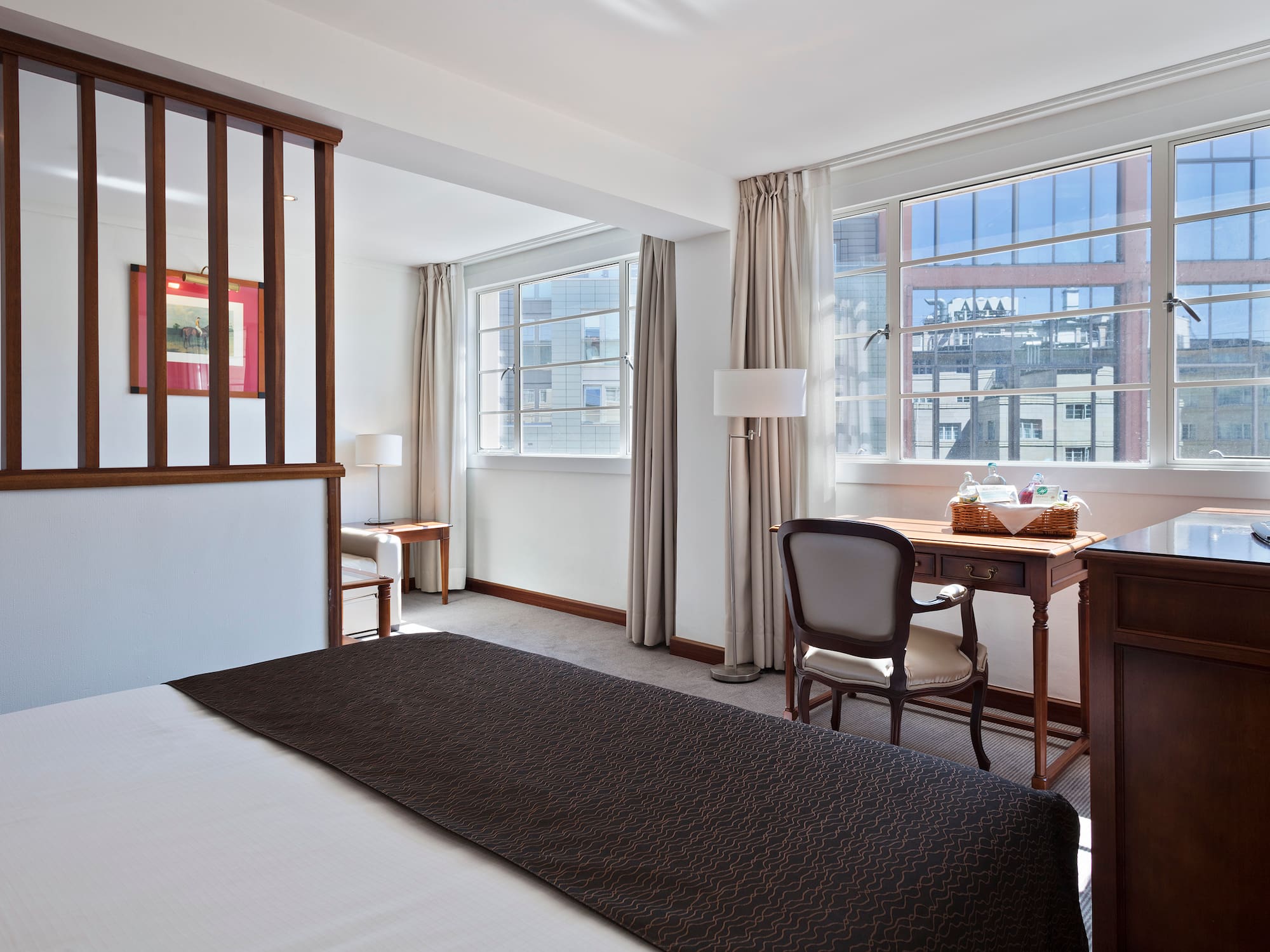 Hotel room with bed, work desk, large windows, and city view.