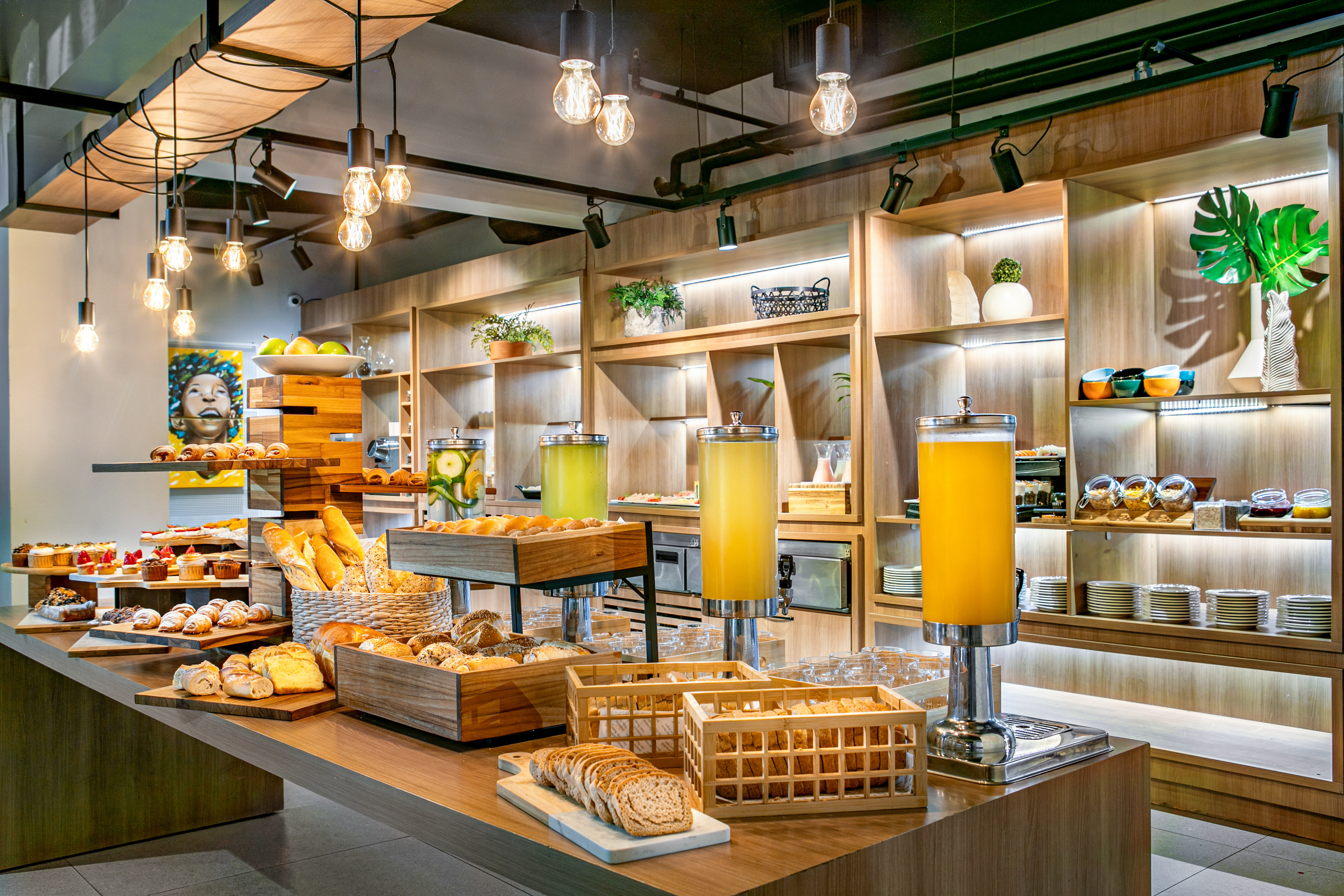 Hotel breakfast buffet with pastries, breads, juices, and modern wood decor.