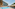 Sunny resort pool with straw umbrellas, loungers, and modern hotel building.