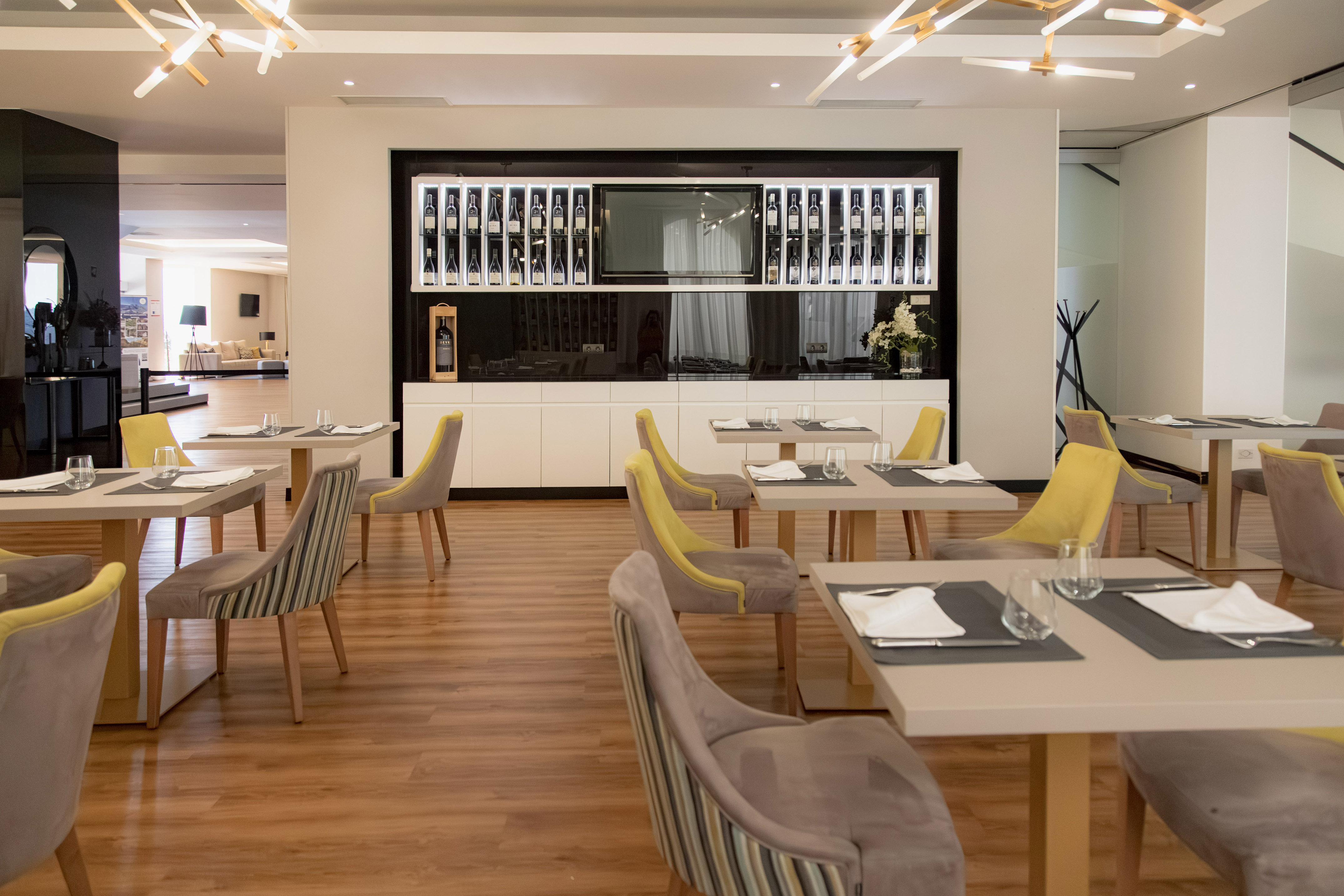 Modern restaurant dining room with set tables, stylish chairs, and a prominent wine display.