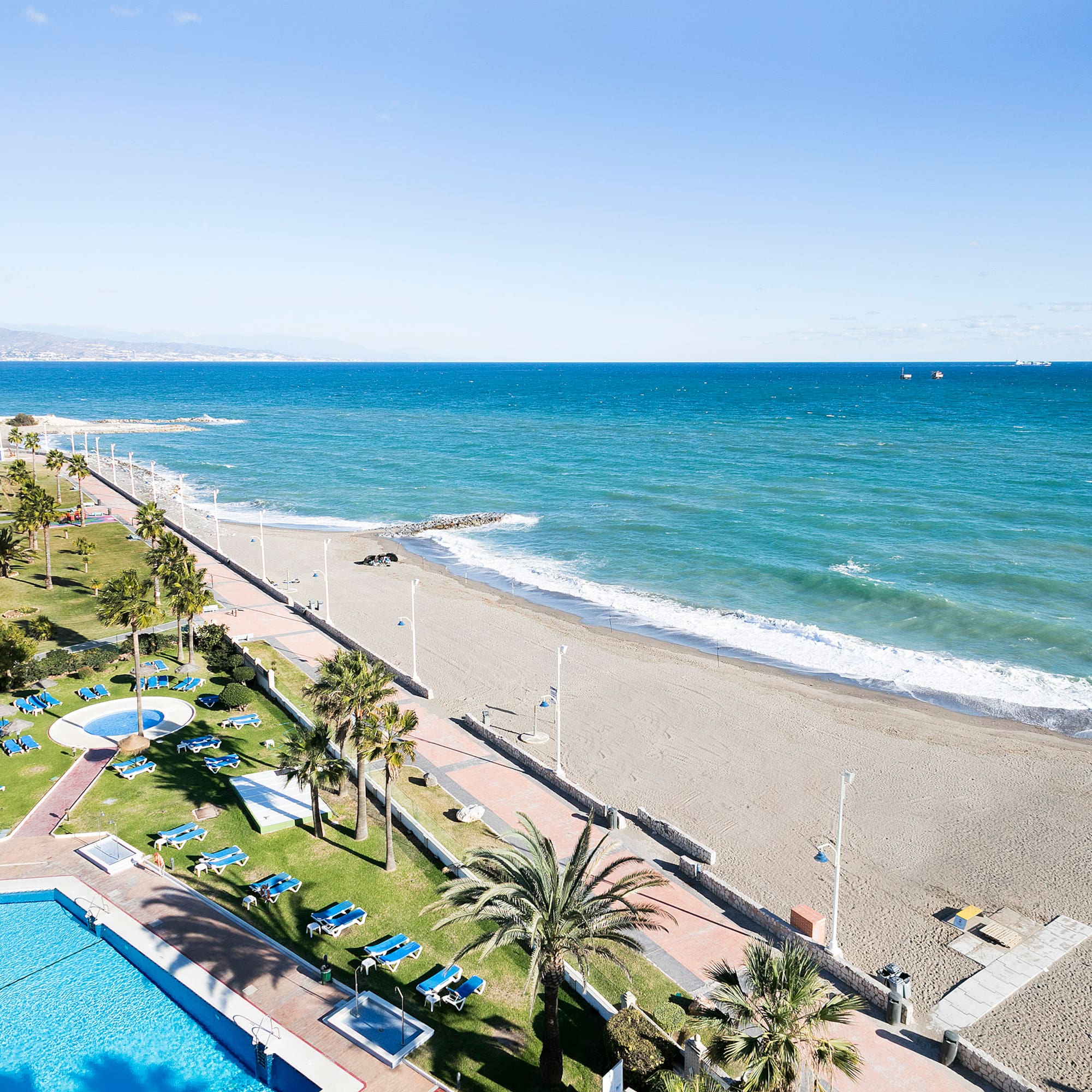 Beachfront resort with pools, palm trees, sandy beach, and blue ocean.