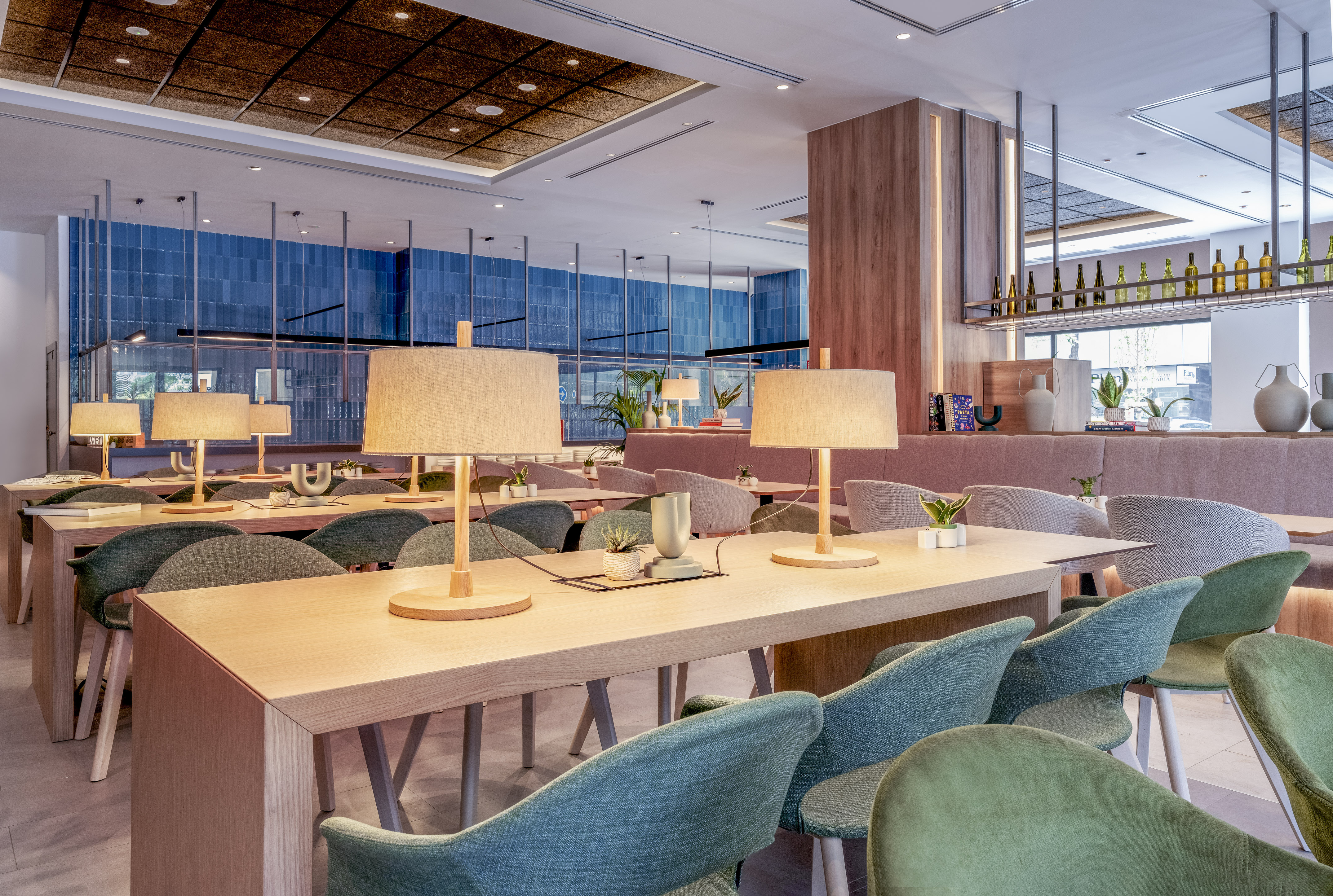 Modern cafe interior with communal tables, lamps, and stylish green chairs.