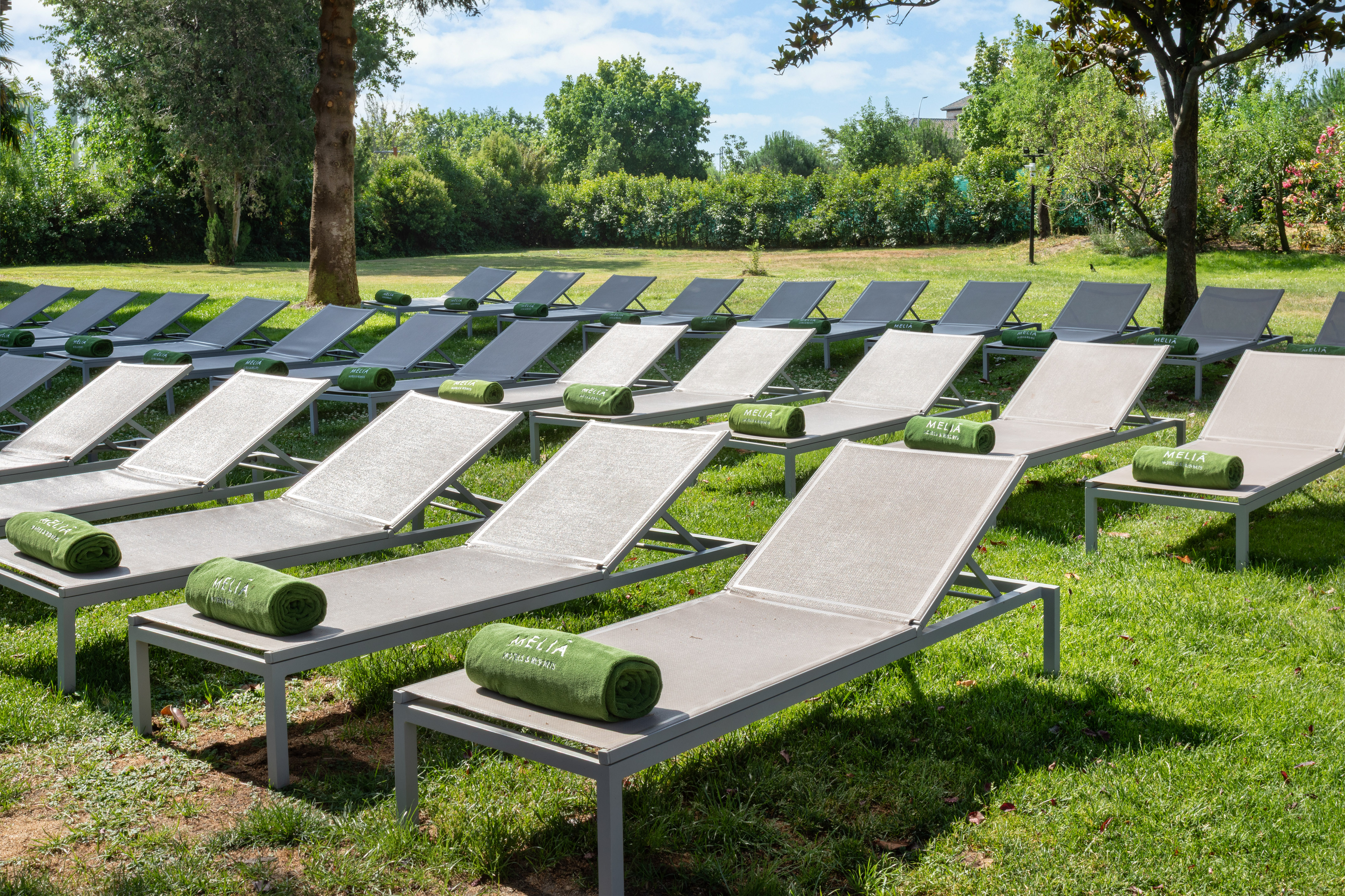 Rows of grey sun loungers with green Meliá towels on a sunny resort lawn.