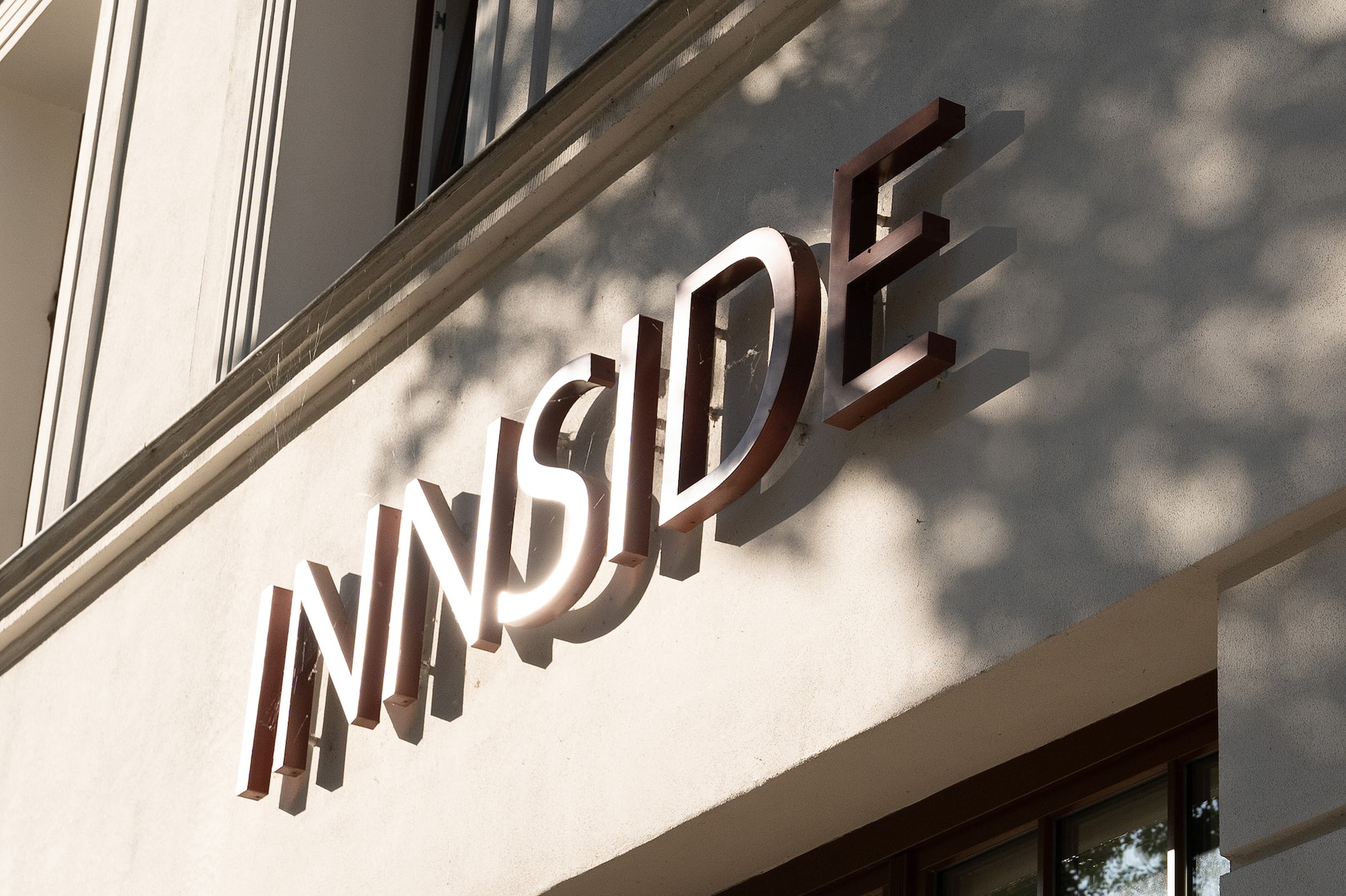 3D 'INNSIDE' sign on white hotel building facade with dappled tree shadows.