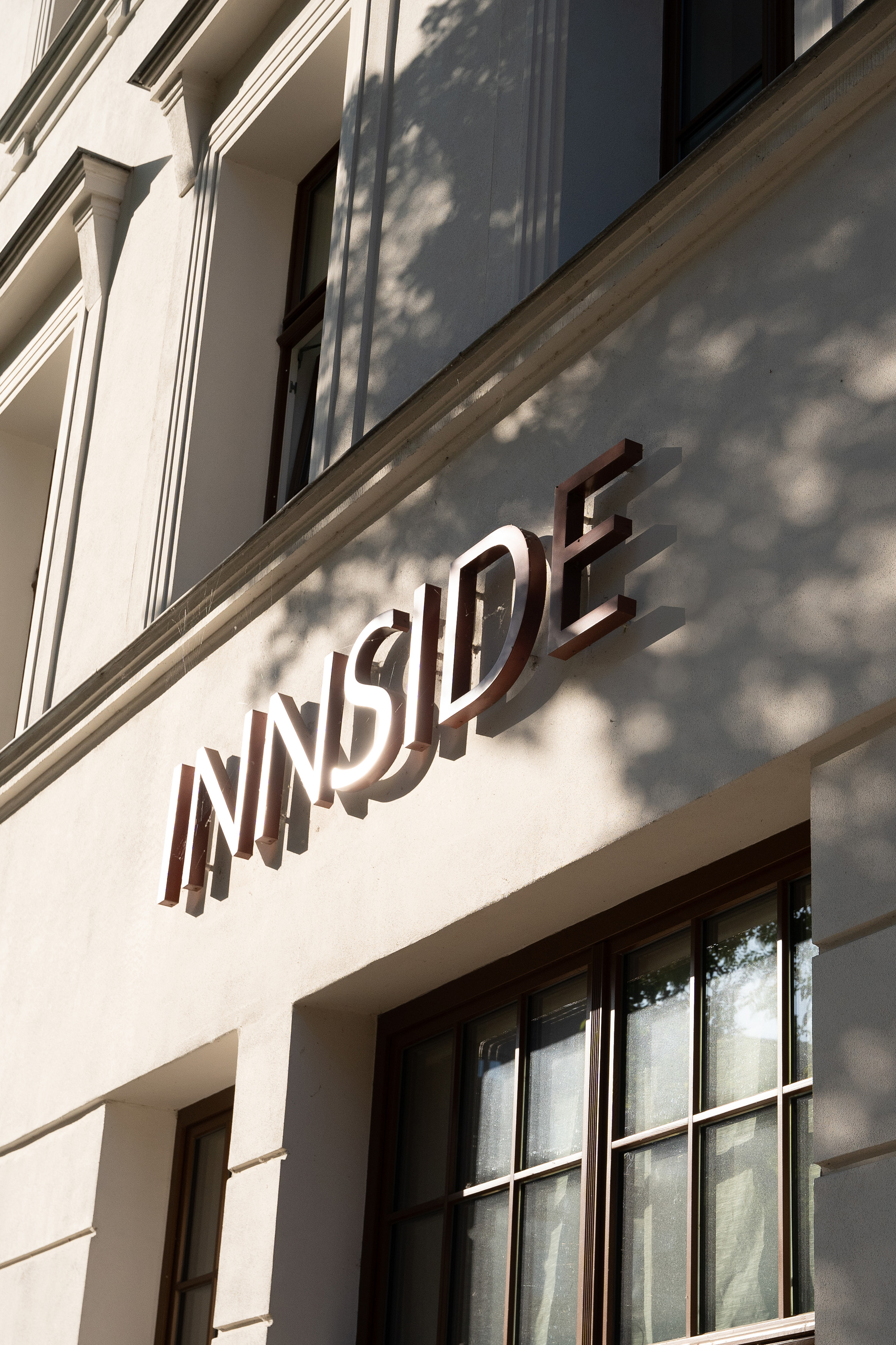 3D 'INNSIDE' sign on white hotel building facade with dappled tree shadows.