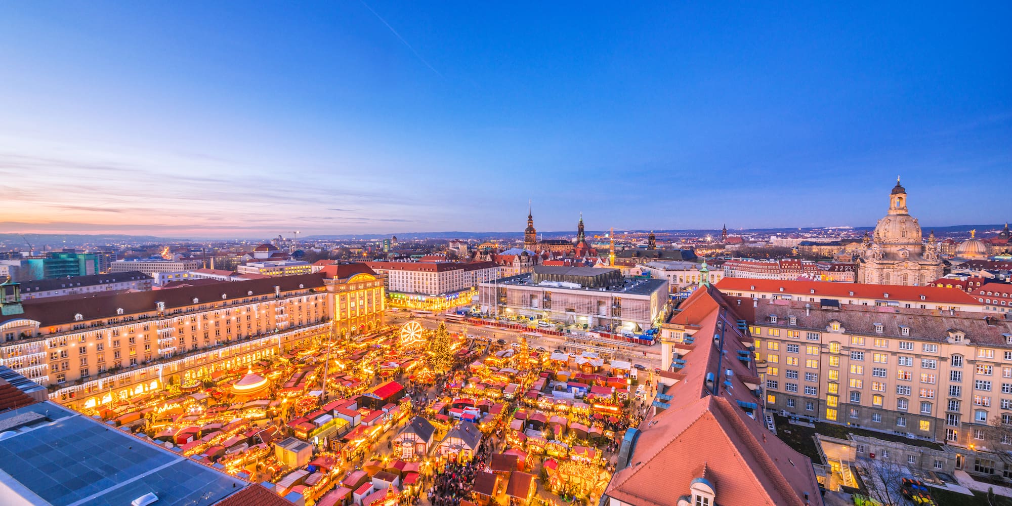 Dresden Striezelmarkt aerial view at dusk with glowing stalls and city lights.