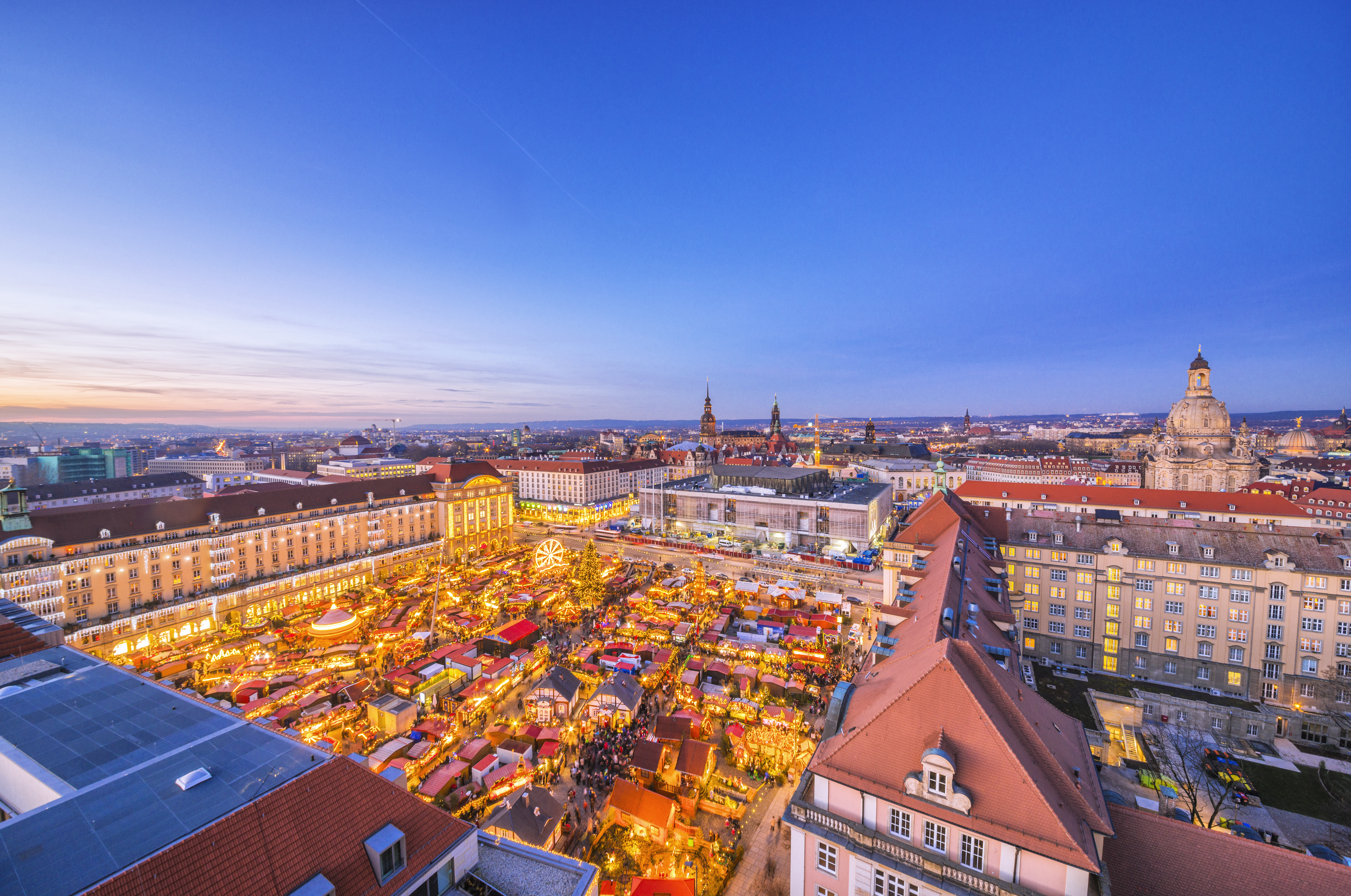 Dresden Striezelmarkt aerial view at dusk with glowing stalls and city lights.