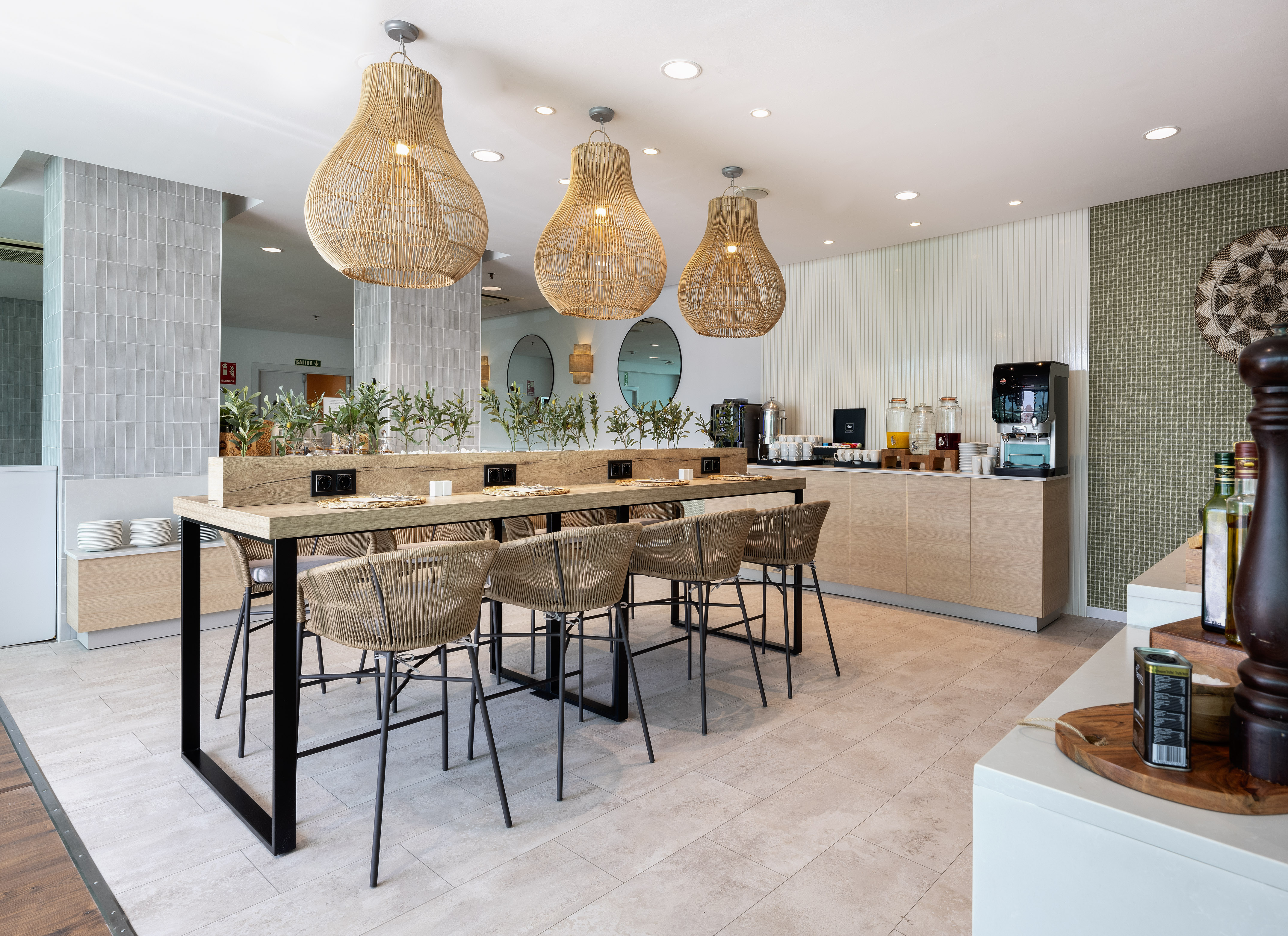 Modern hotel breakfast room with communal table, woven seating, buffet.