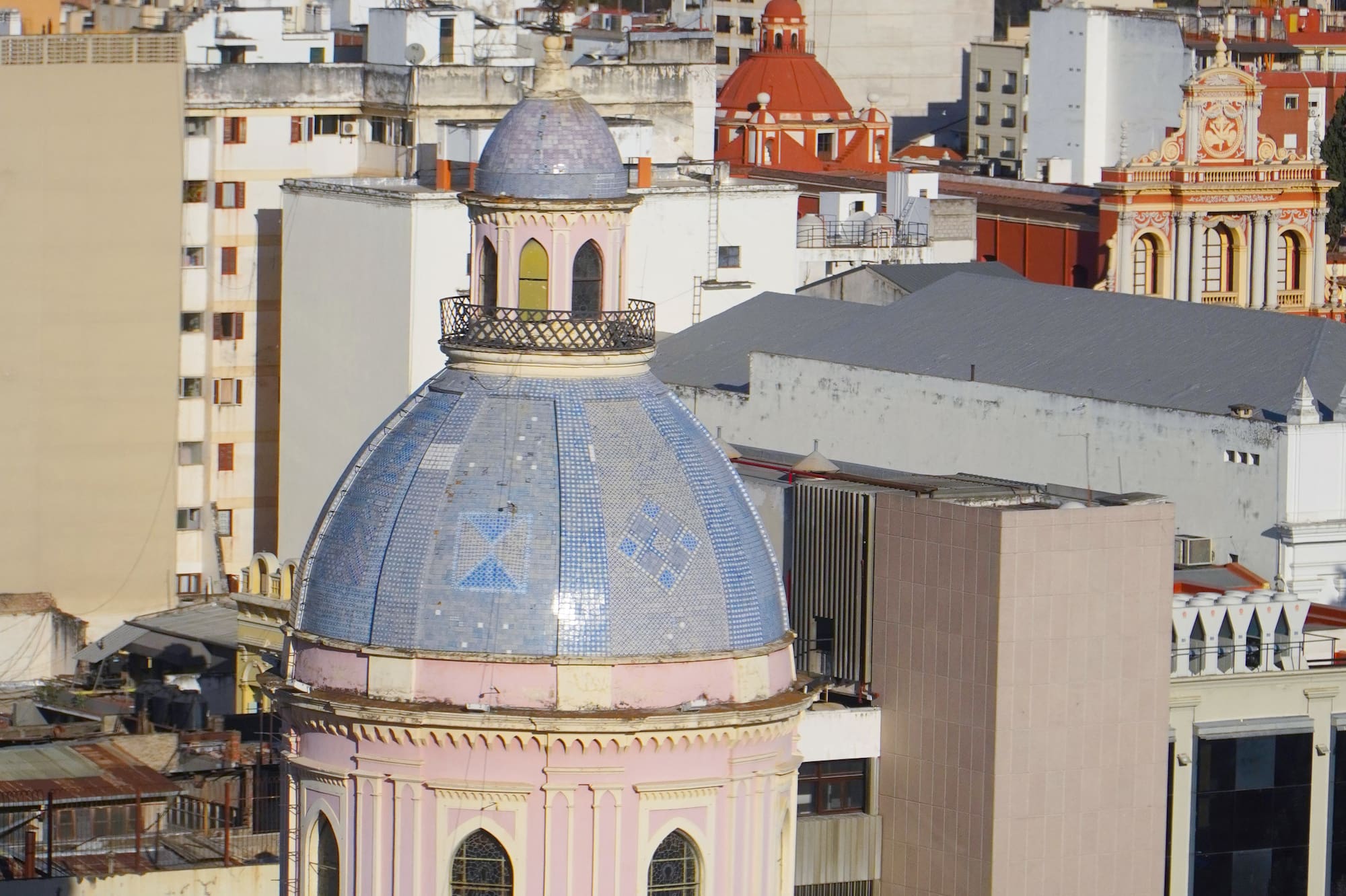 Large blue tiled dome with pink base, cityscape, and distant green mountains.