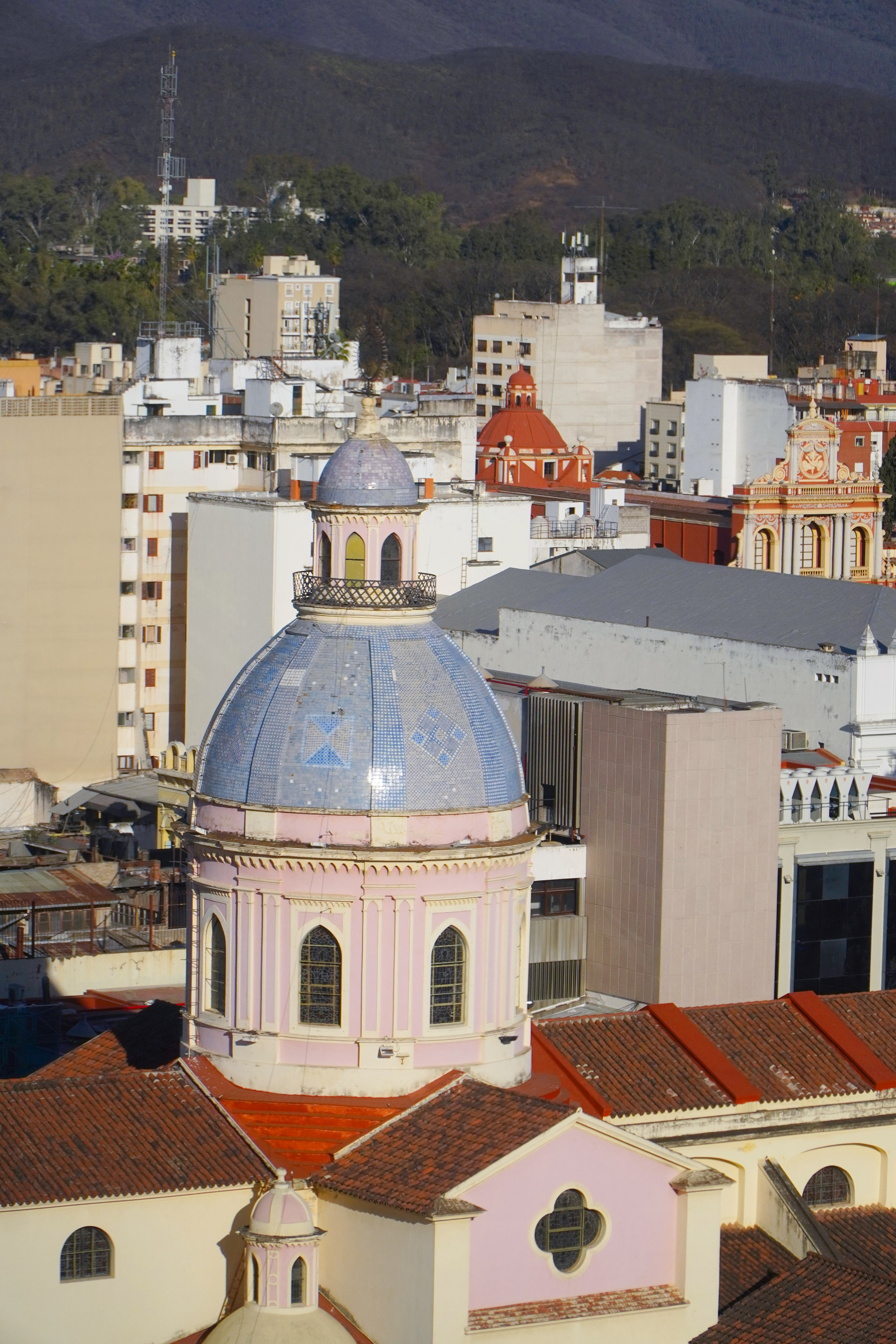 Large blue tiled dome with pink base, cityscape, and distant green mountains.