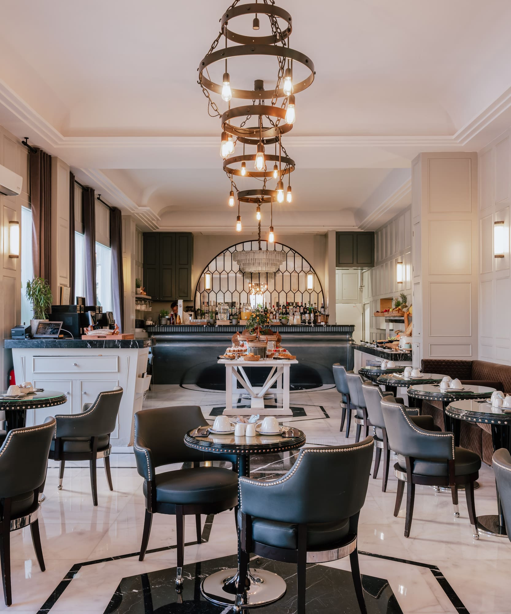 Luxury hotel breakfast area with marble floor, ornate chandelier, and buffet.