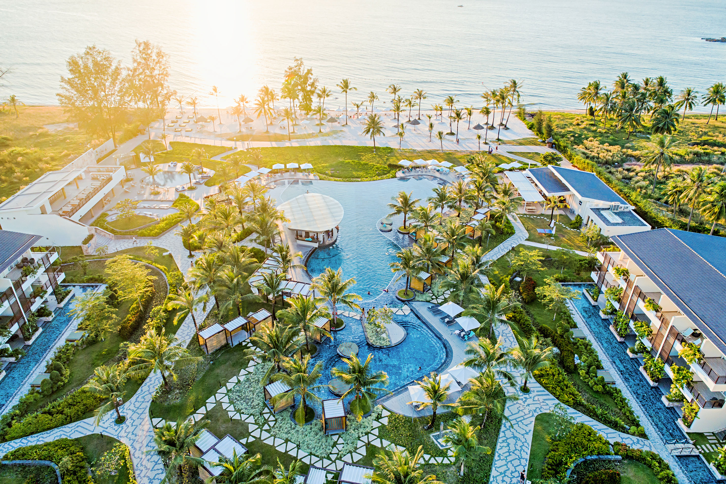 Aerial view: luxury tropical beachfront resort, large pool, palm trees, ocean.