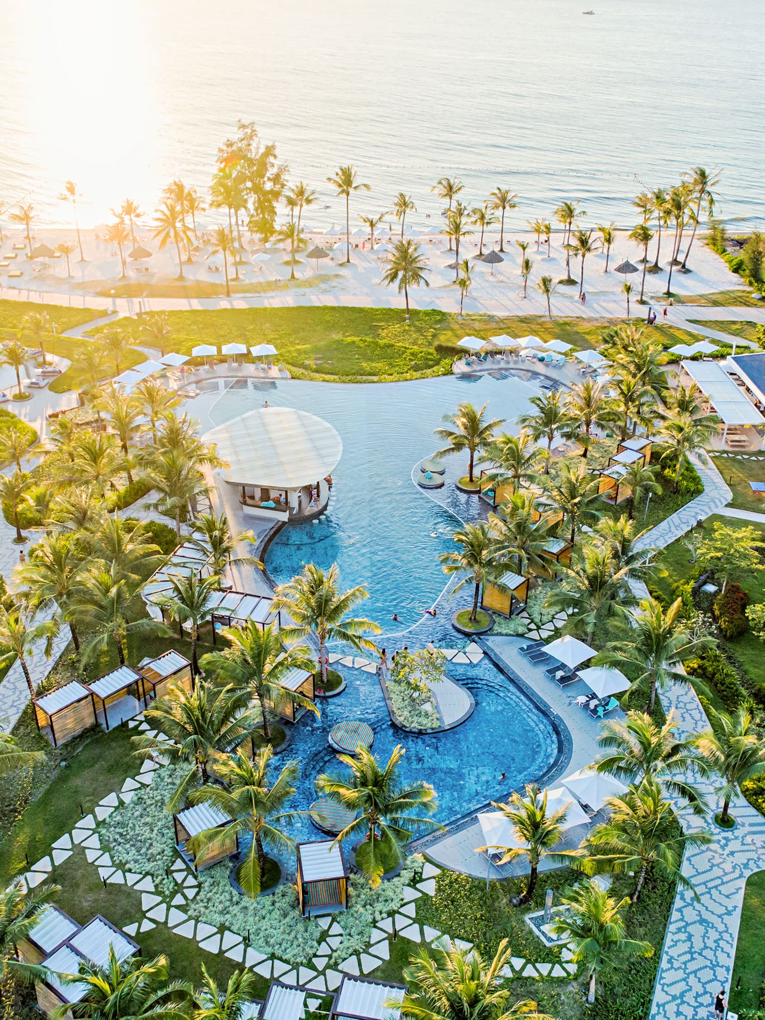 Aerial view: luxury tropical beachfront resort, large pool, palm trees, ocean.