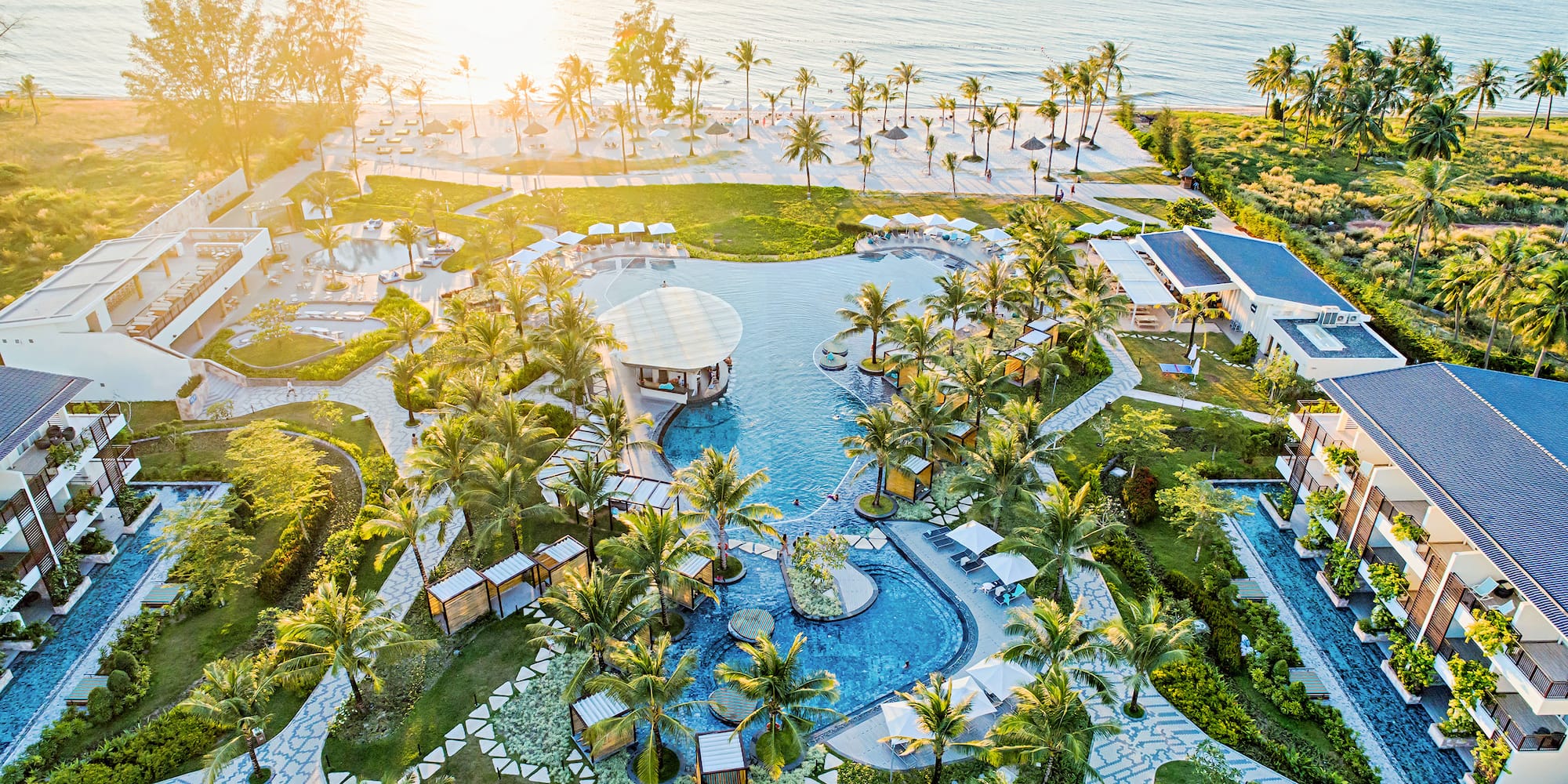 Aerial view: luxury tropical beachfront resort, large pool, palm trees, ocean.