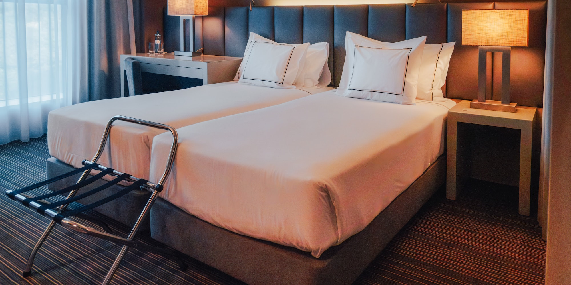 Hotel room with twin beds, lit bedside lamps, and luggage rack.