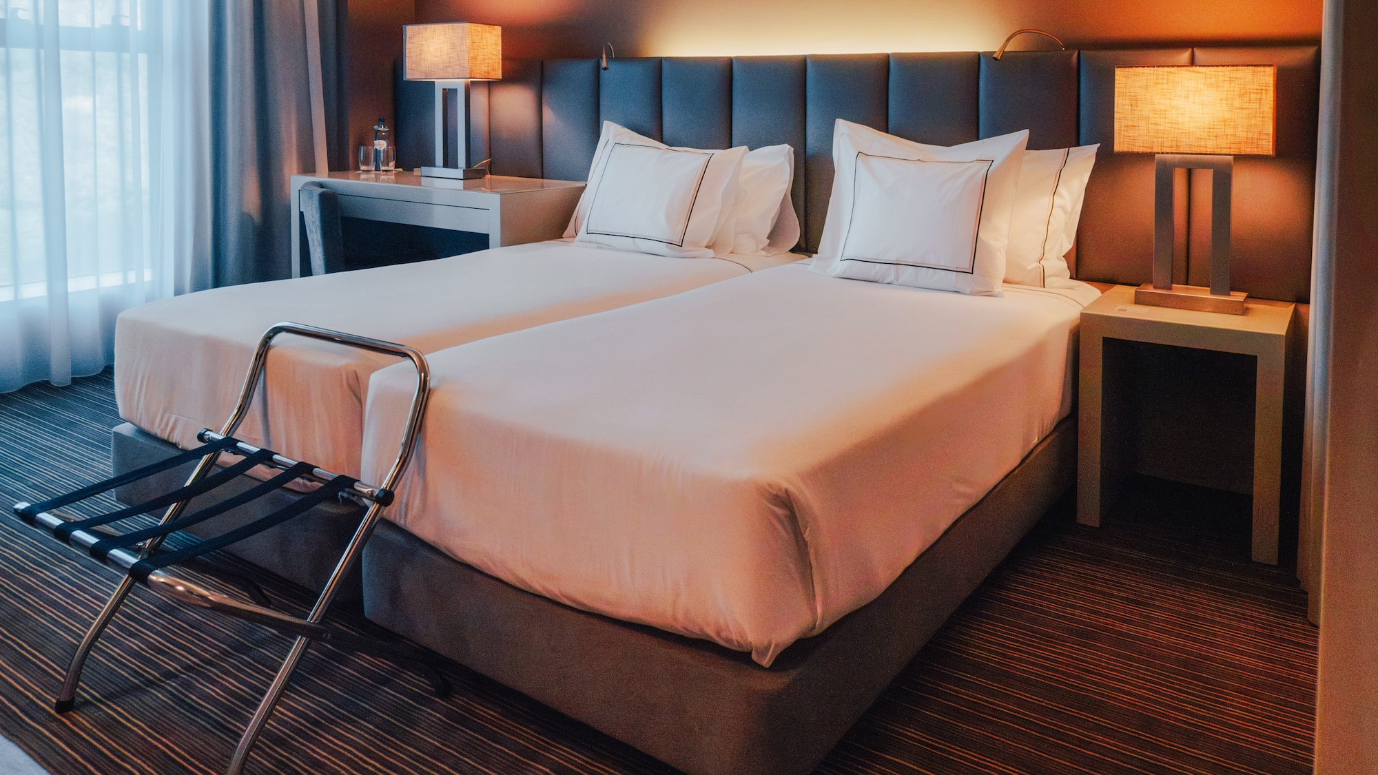 Hotel room with twin beds, lit bedside lamps, and luggage rack.