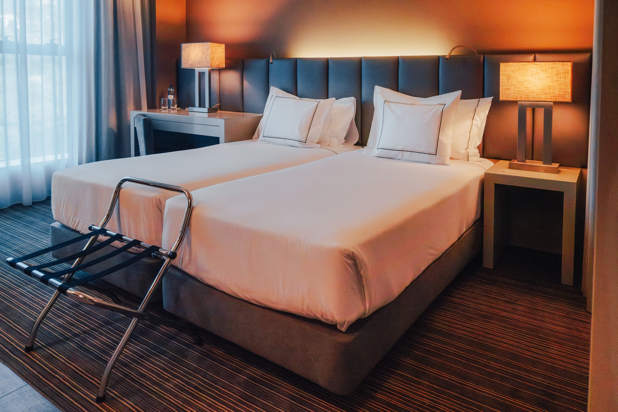 Hotel room with twin beds, lit bedside lamps, and luggage rack.