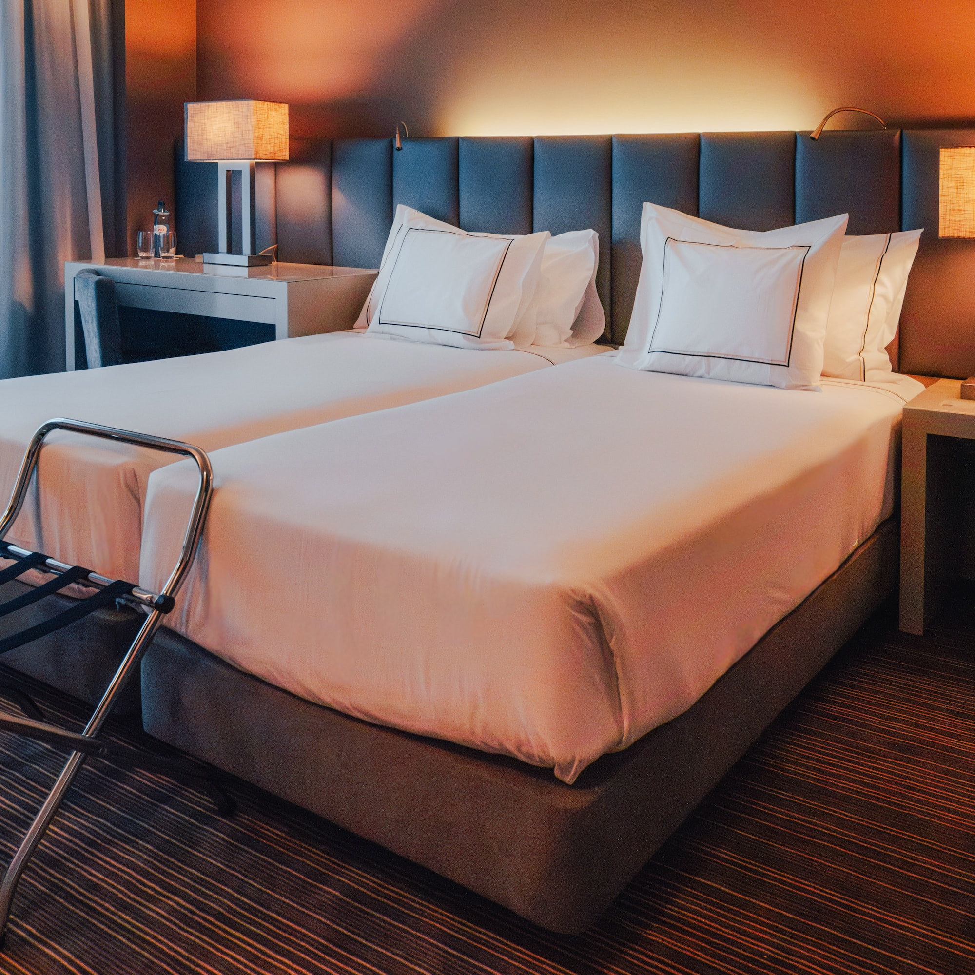 Hotel room with twin beds, lit bedside lamps, and luggage rack.