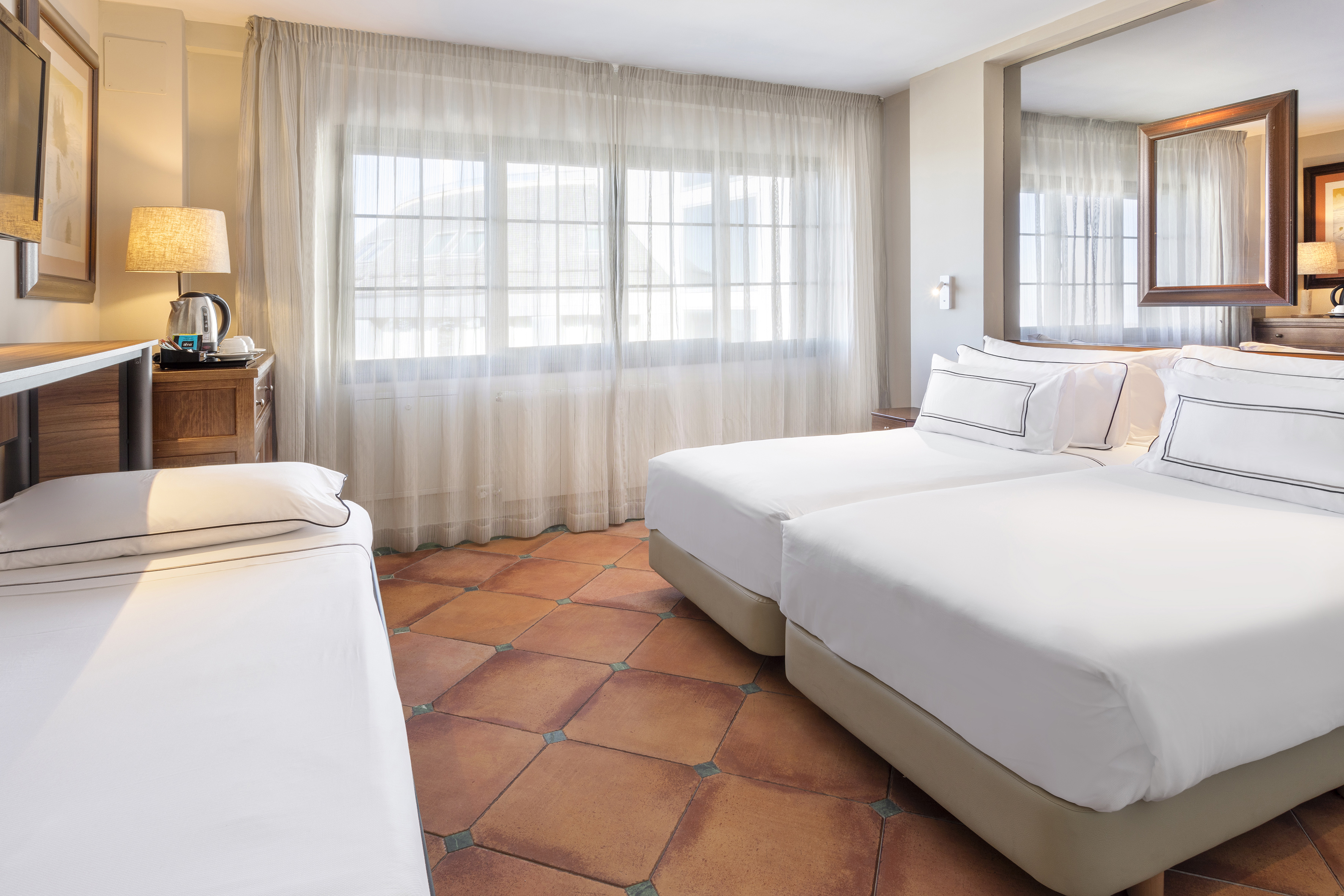 Guest room with twin beds, single bed, terracotta tiled floor, and window.