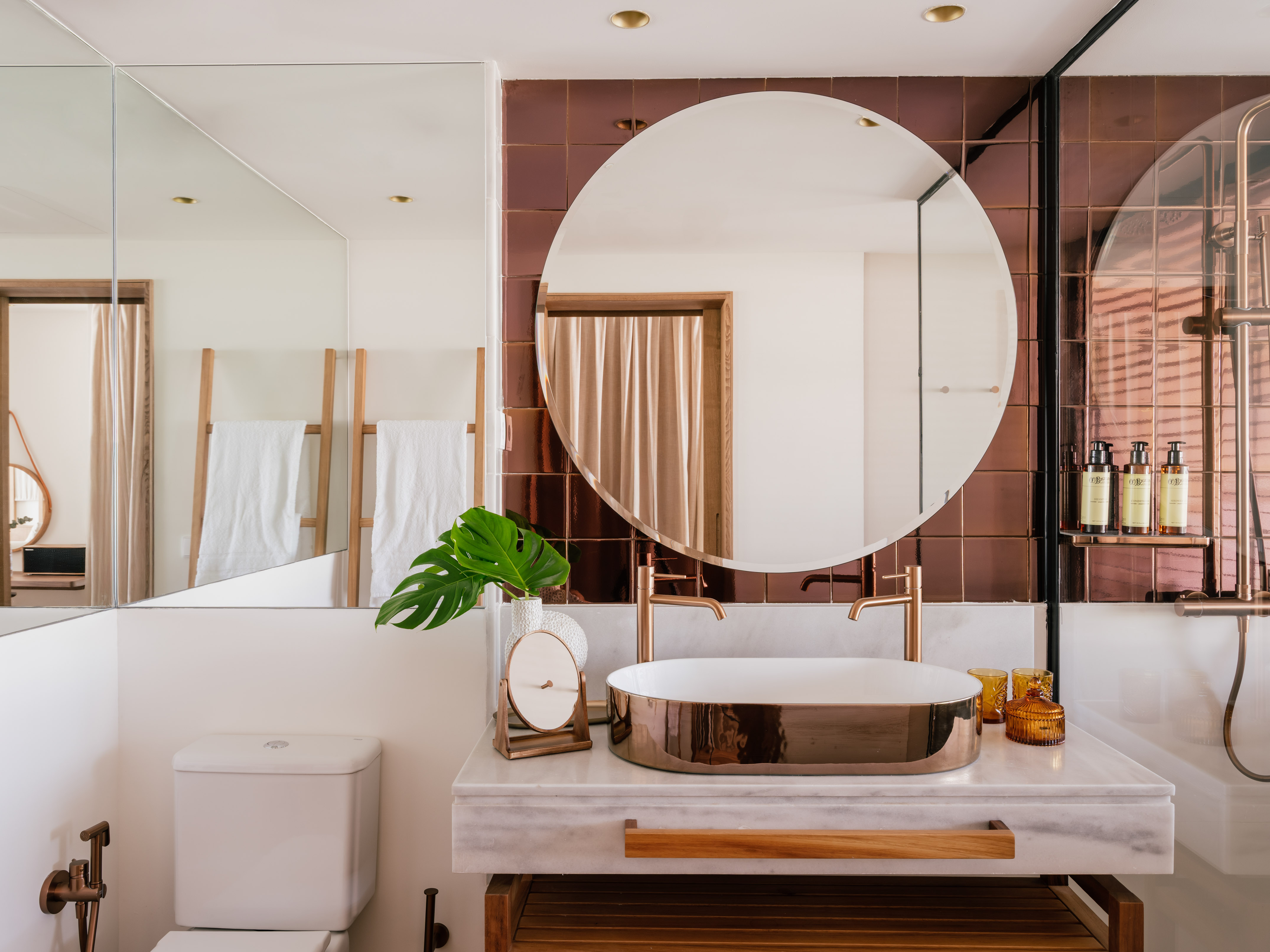 Modern bathroom with rose gold basin, circular mirror, copper tiles, marble vanity.