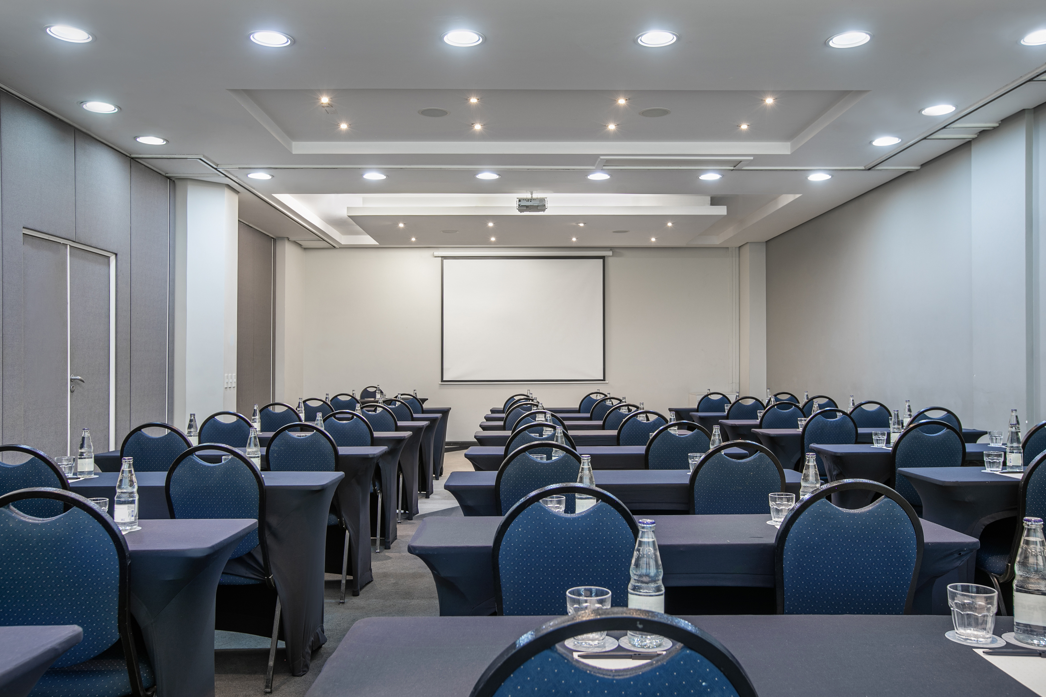 Spacious conference room with blue chairs, dark tables, and a large projection screen.